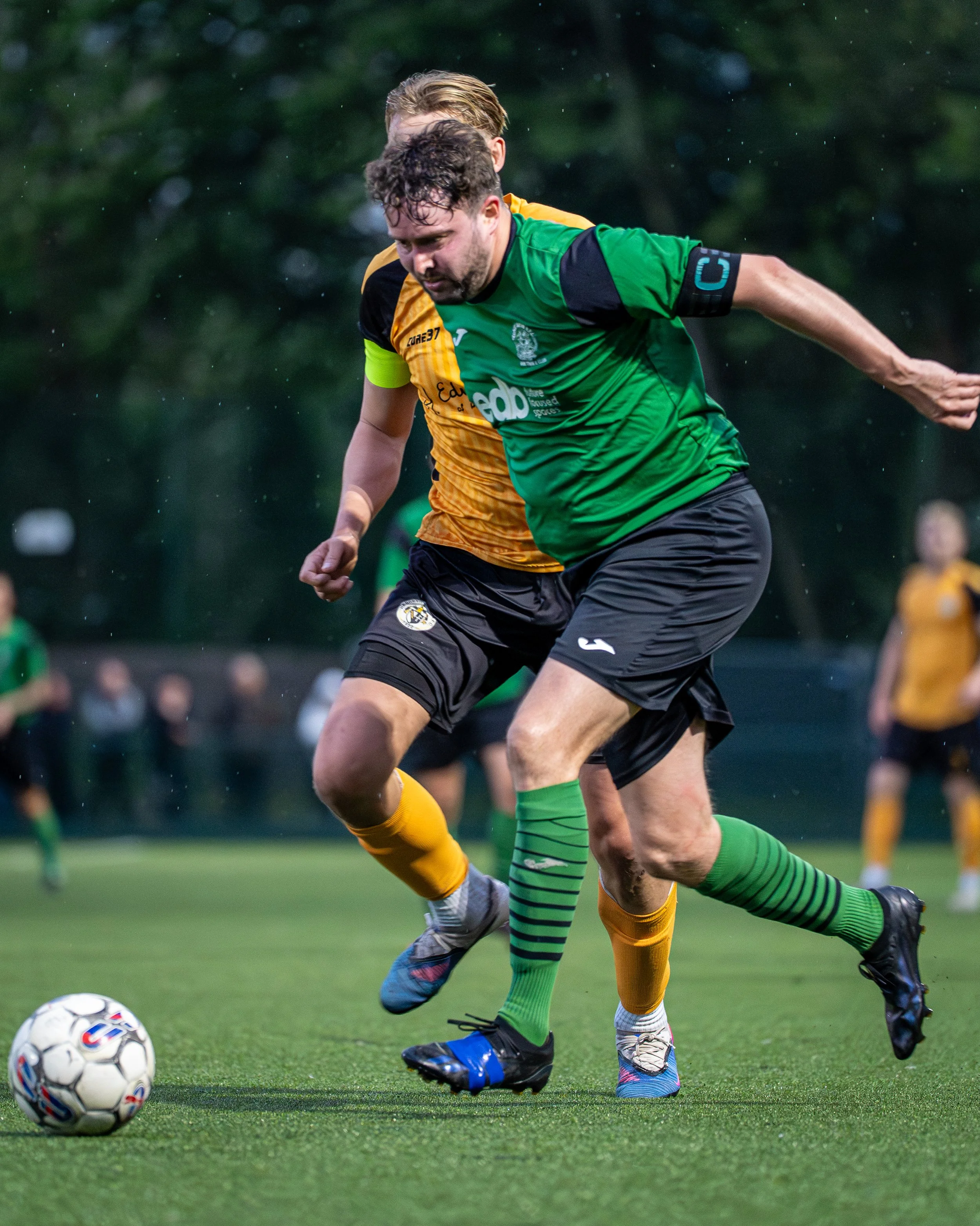 Two soccer players fighting for the ball on the field during a game, with the focus on their legs and feet.