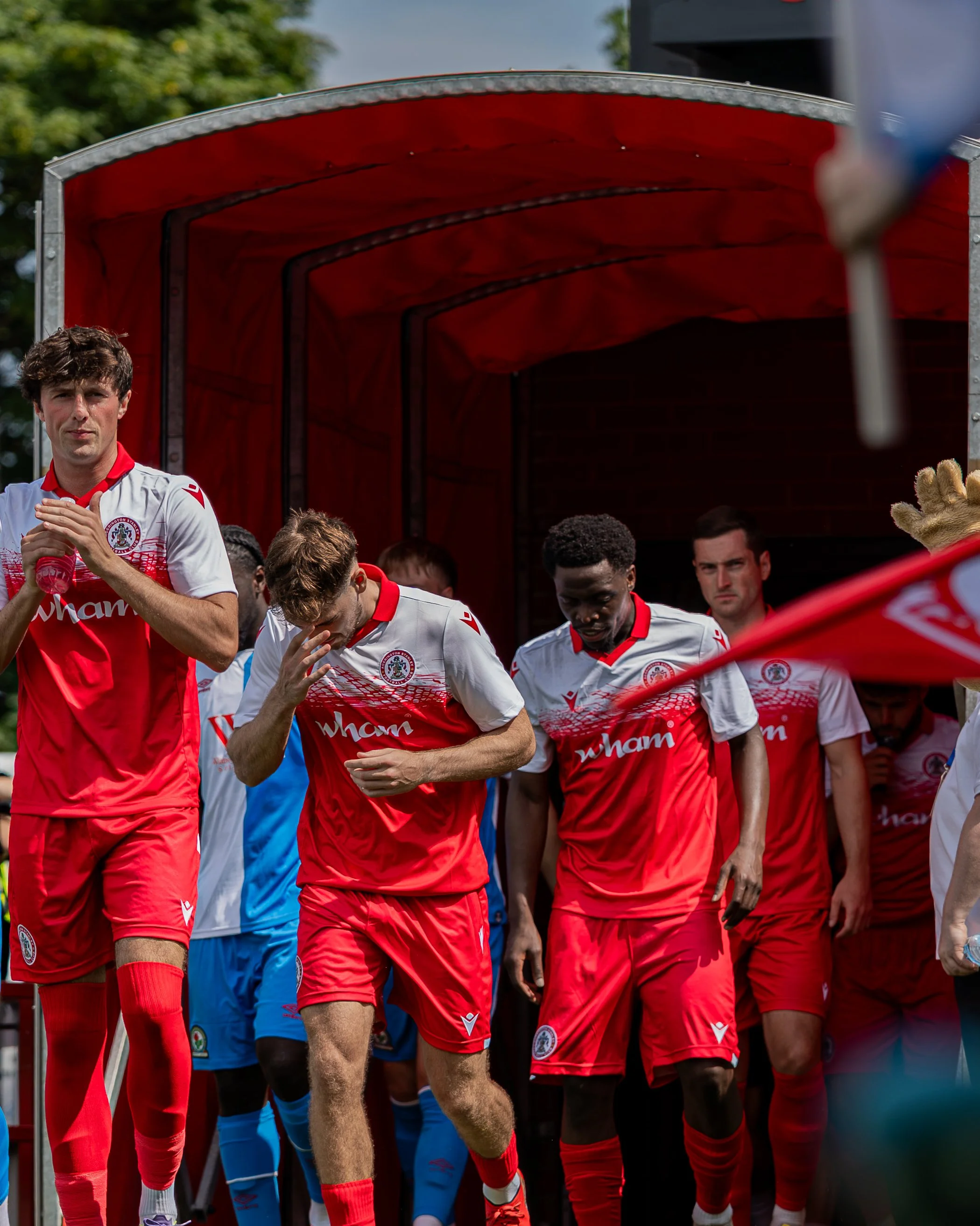 Soccer players wearing white and red jerseys walking out of a tunnel onto the field before a game.