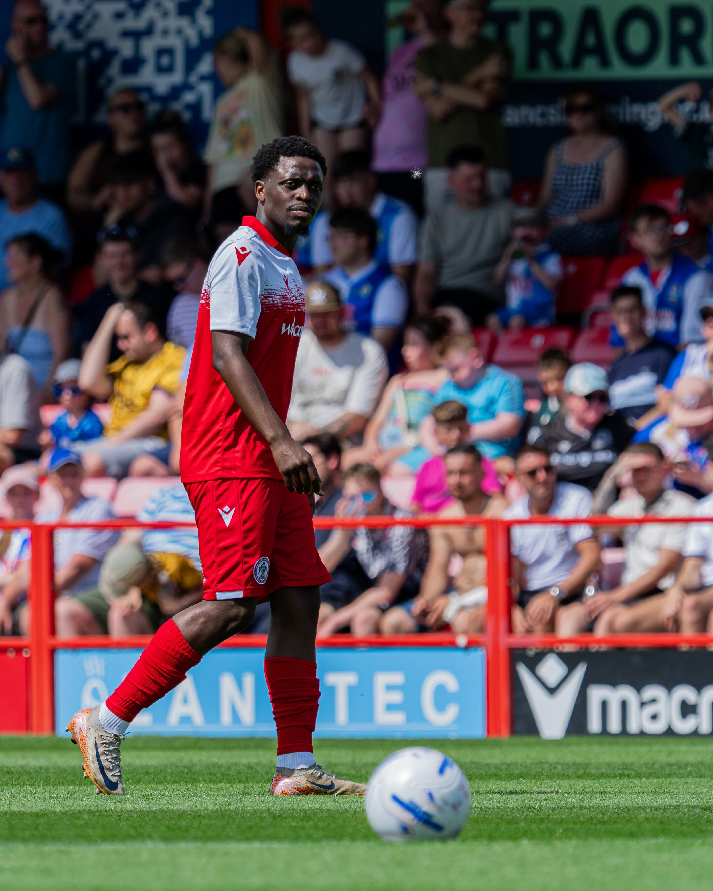 A soccer player in red and white uniform preparing to kick a ball during a match with spectators in the background.