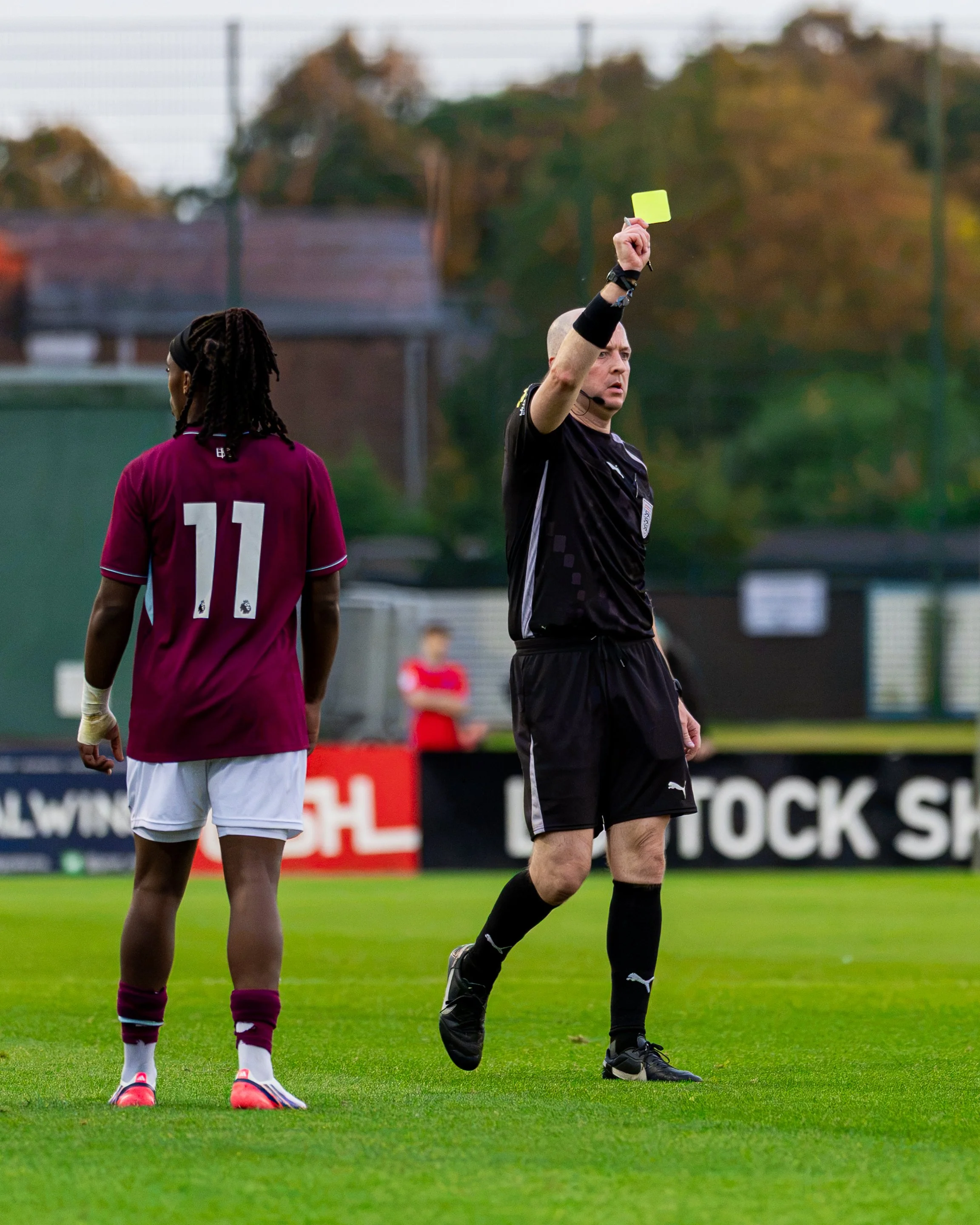 A soccer referee showing a yellow card to a player on the field, with another player standing nearby.