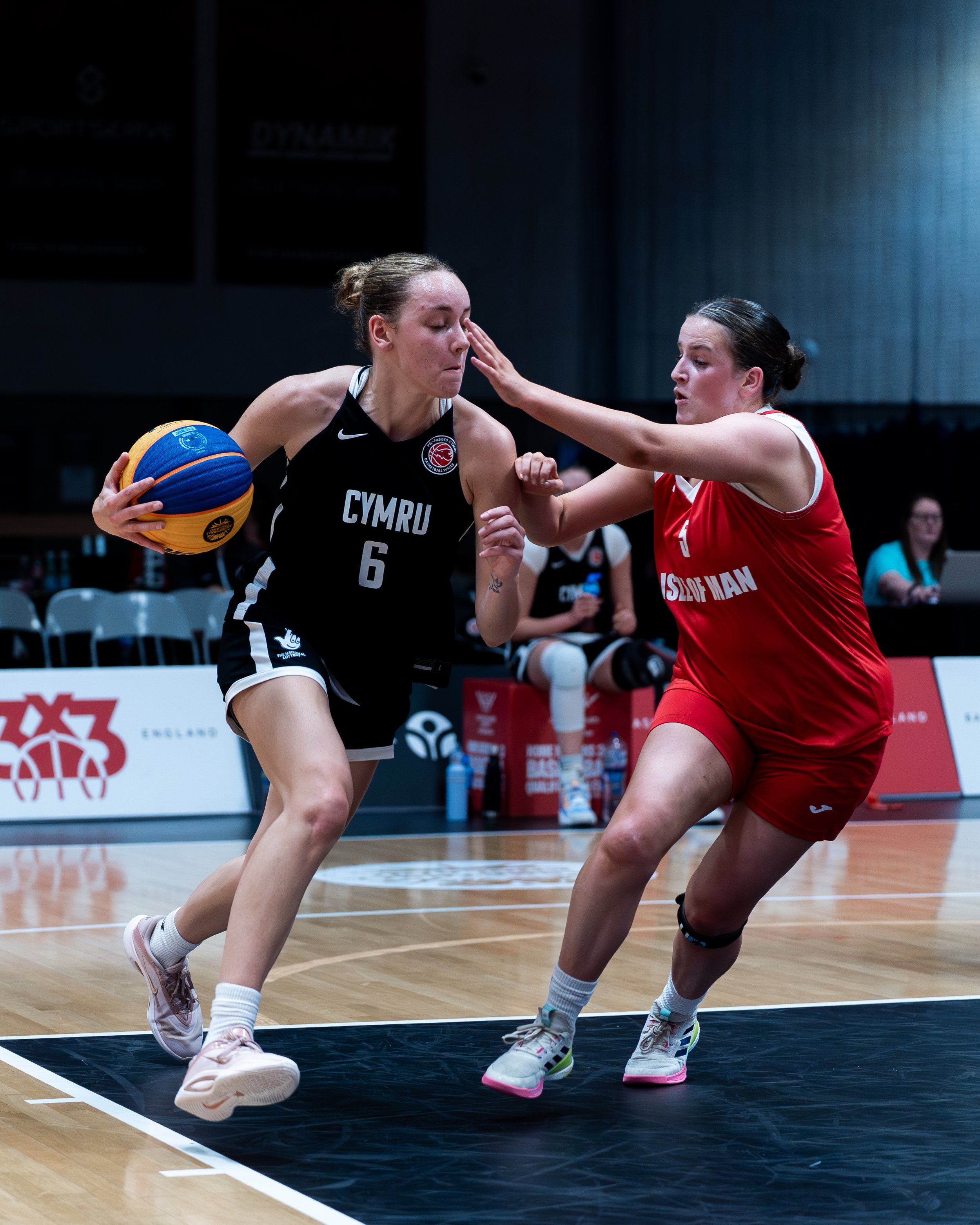 Two female basketball players in black and red jerseys competing for the ball on a basketball court.