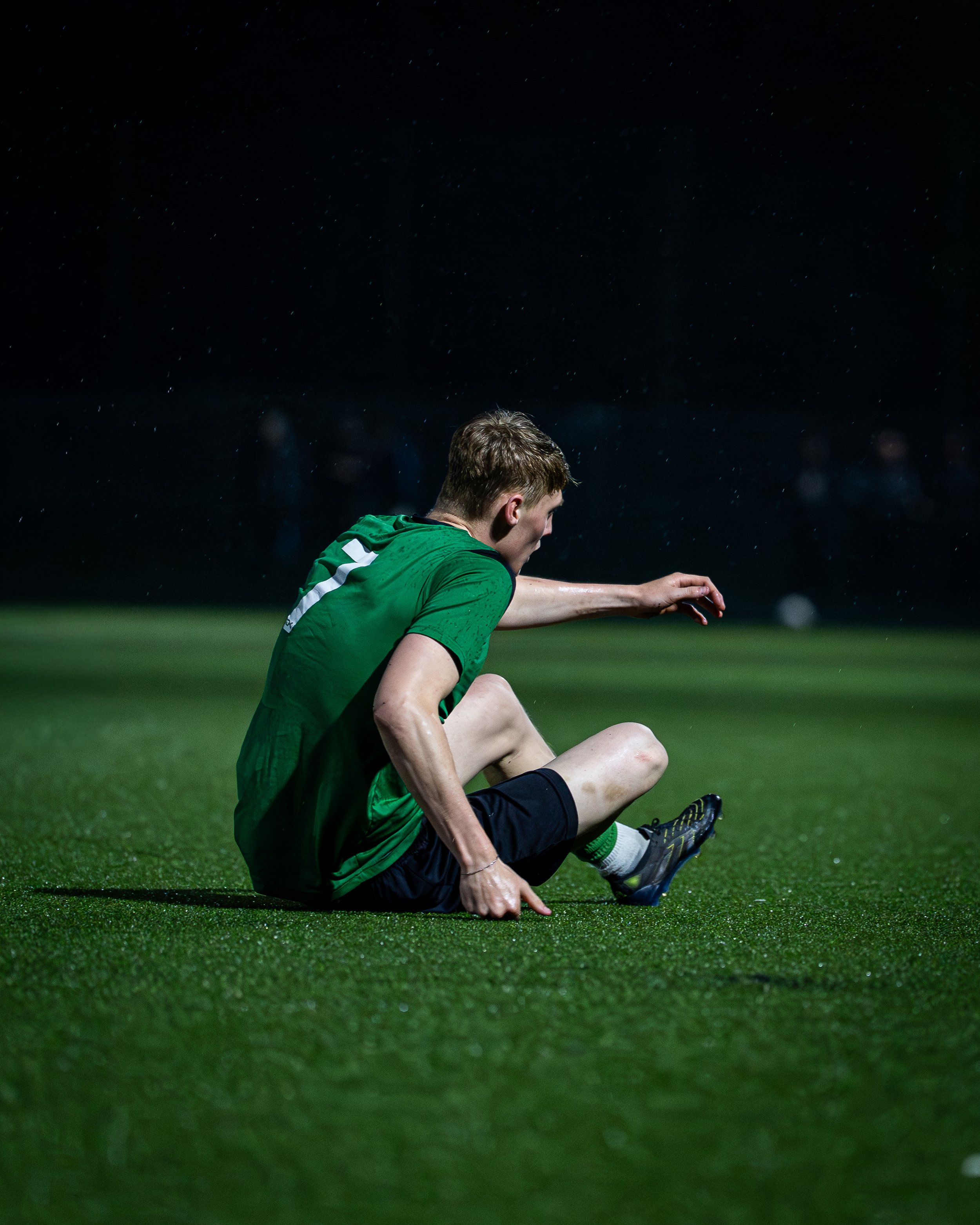A soccer player in a green jersey sitting on a field under the night sky, with stars visible above.