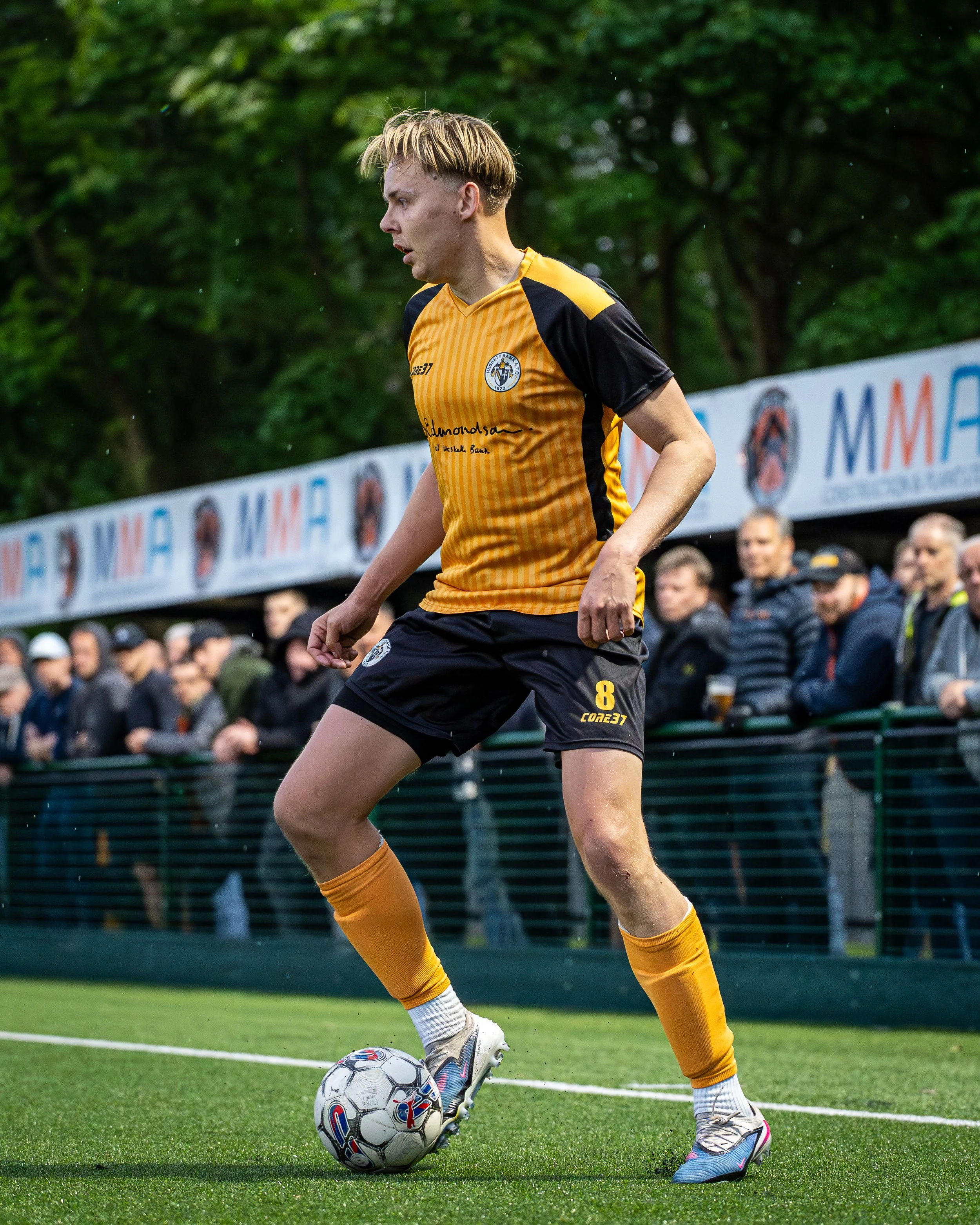 A female soccer player in a yellow and black uniform dribbling a soccer ball on a green field during a match.