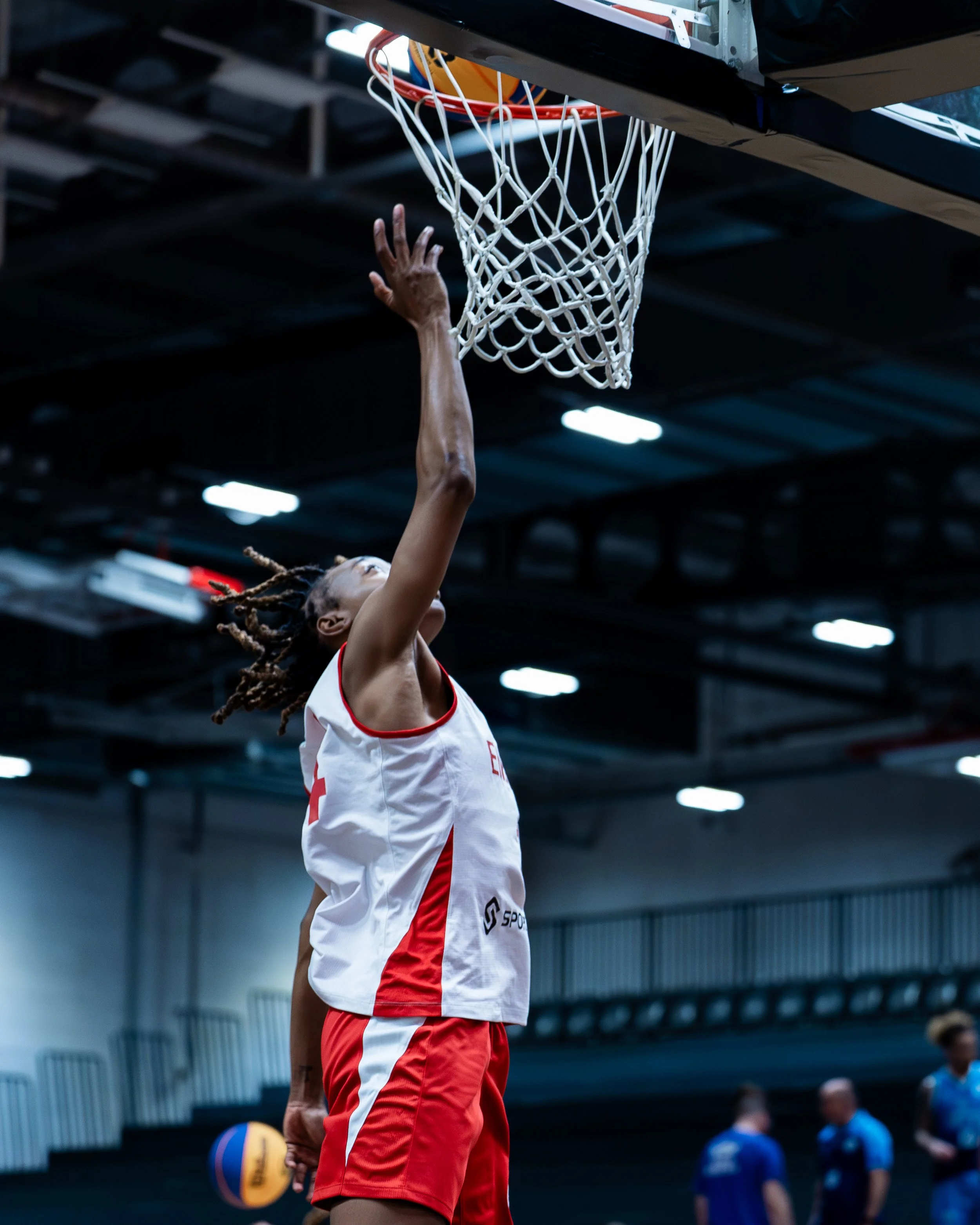 A basketball player jumping towards the basketball hoop during a game, holding a basketball in one hand.
