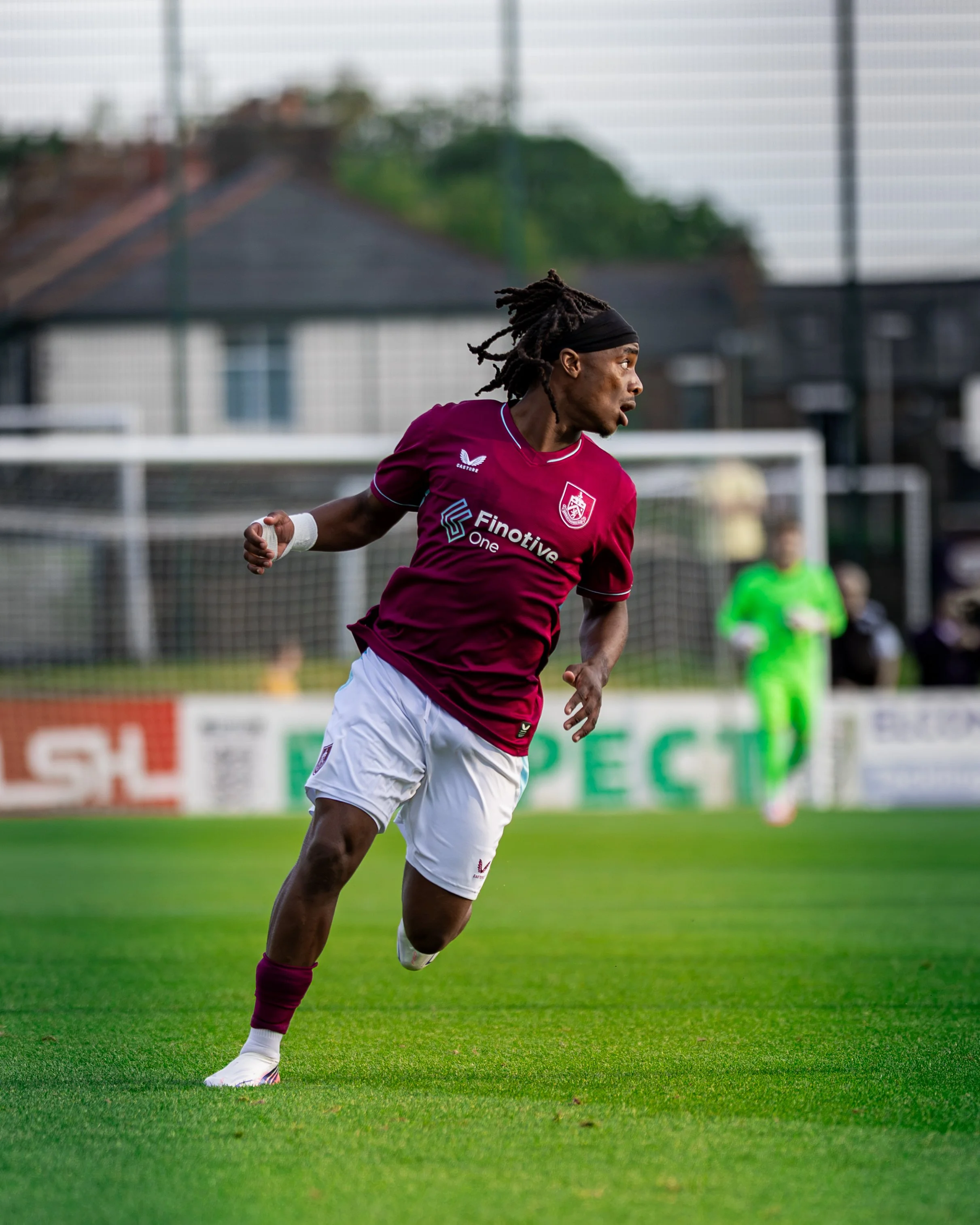 A male soccer player with dreadlocks, wearing a maroon jersey and white shorts, running on a soccer field during a game.