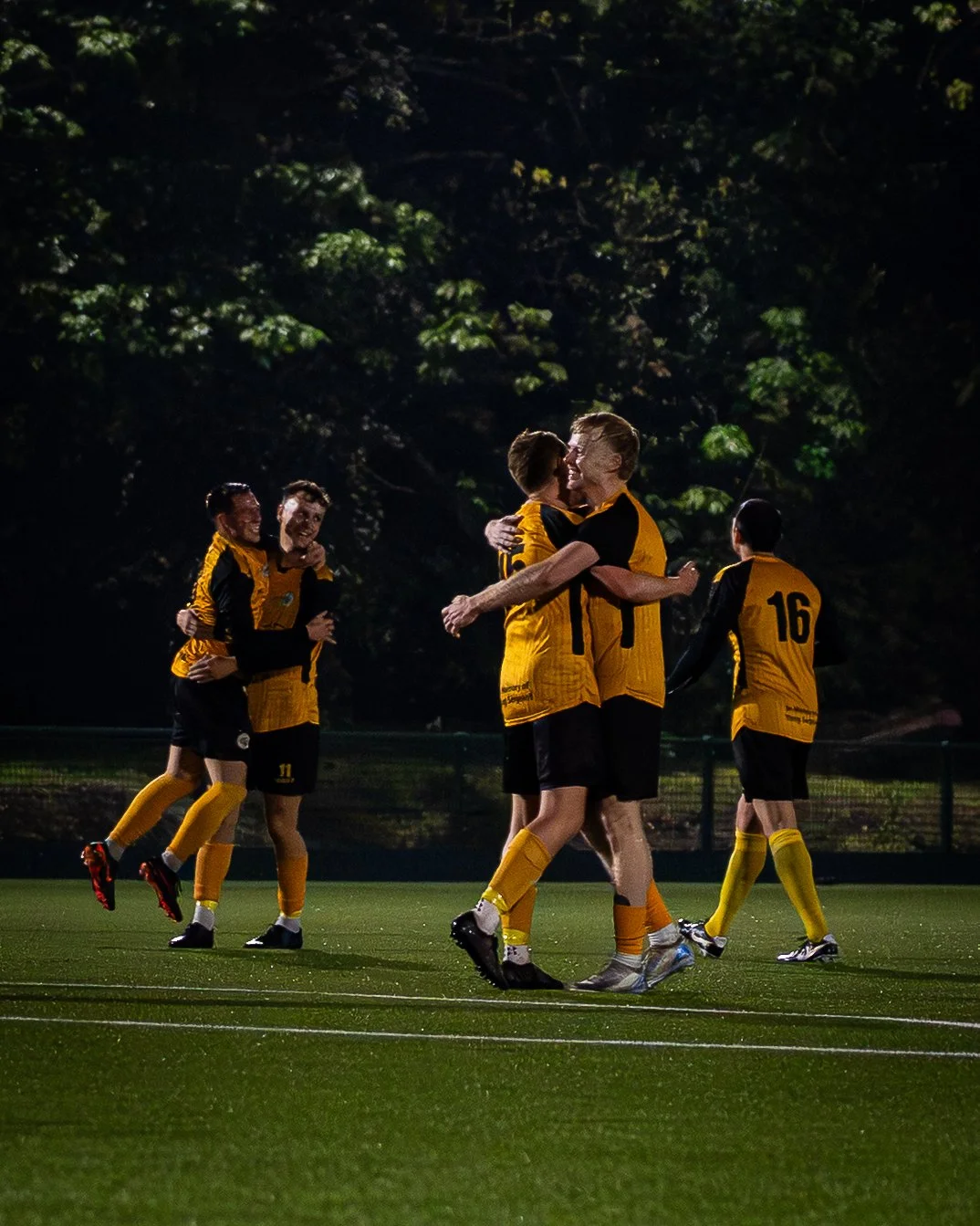 Soccer players in yellow and black uniforms celebrating on the field at night.