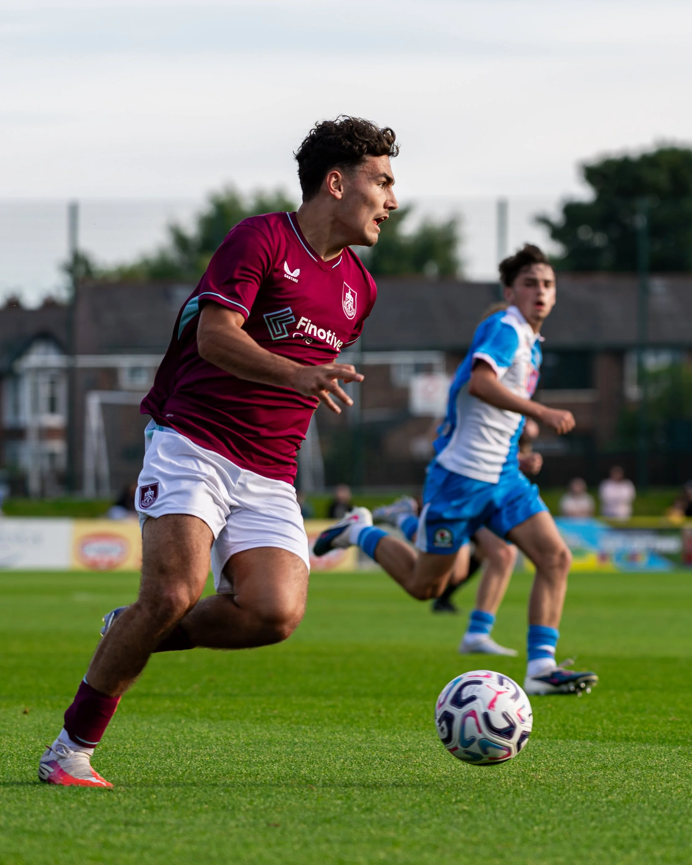 Young male soccer player in maroon jersey running on field with a soccer ball.