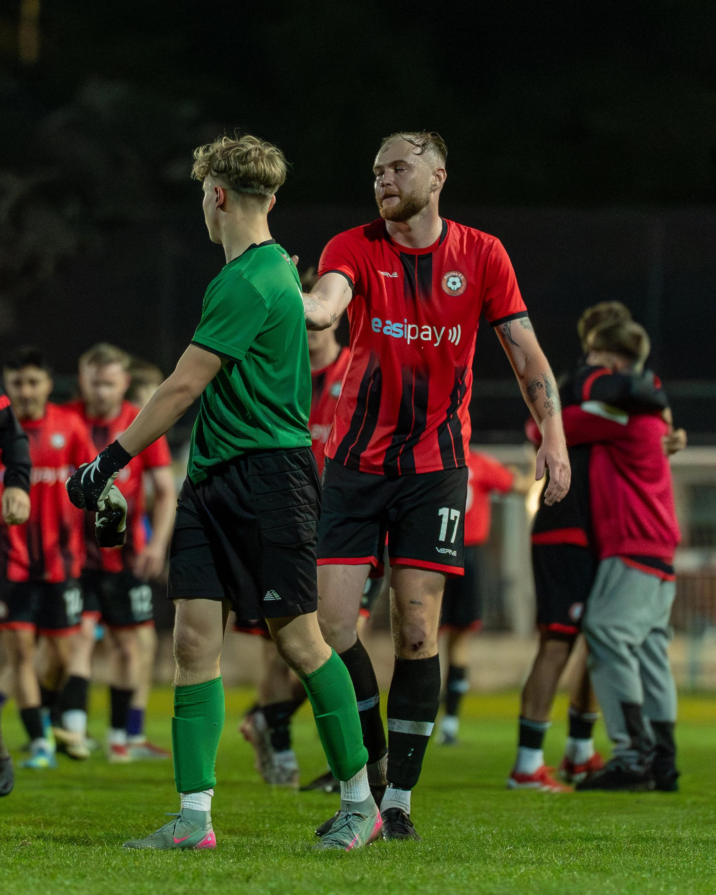 Two soccer players share a moment of interaction during a game, with other players in the background.
