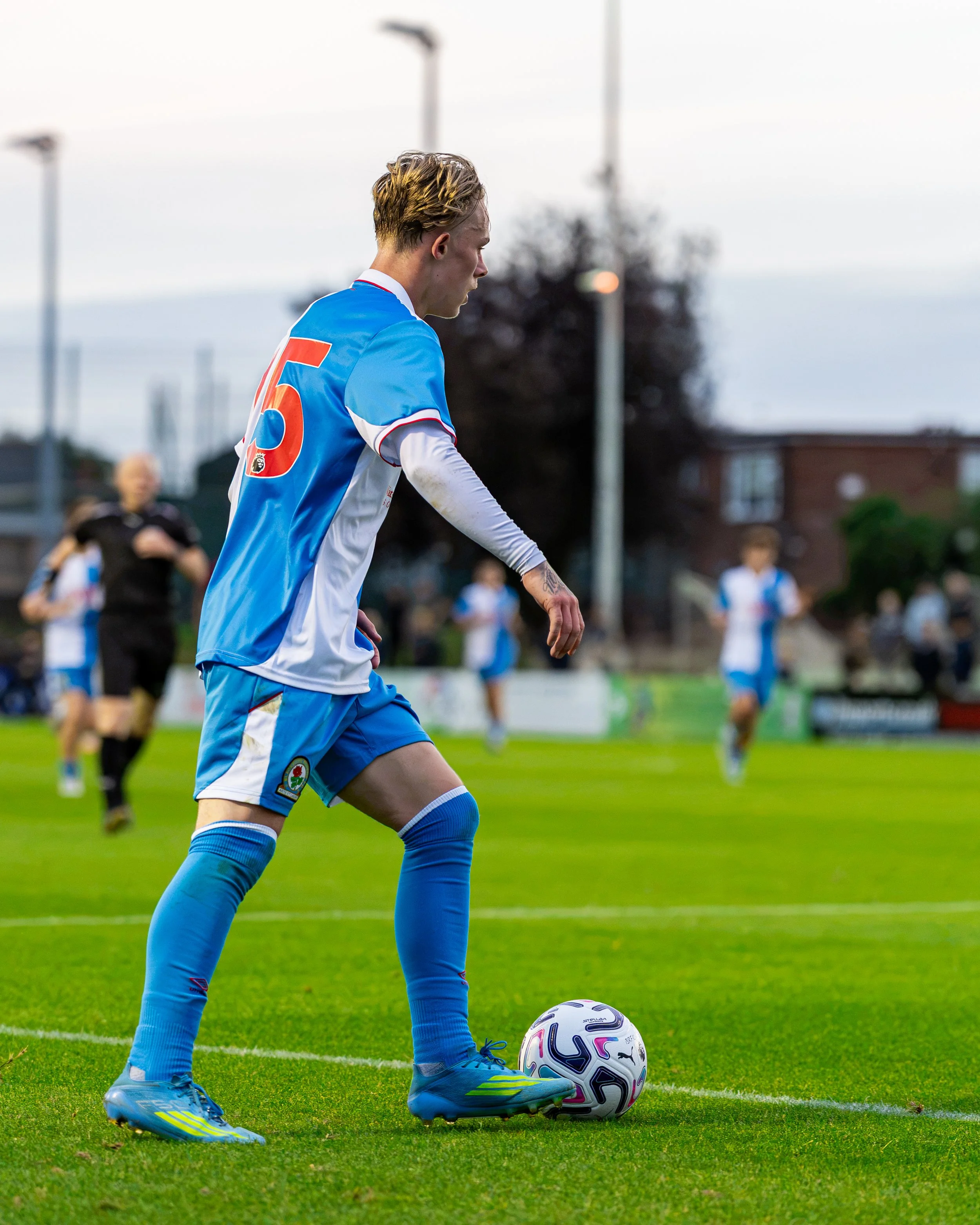Soccer player preparing to kick a ball on the field, wearing a blue and white uniform with number 5.