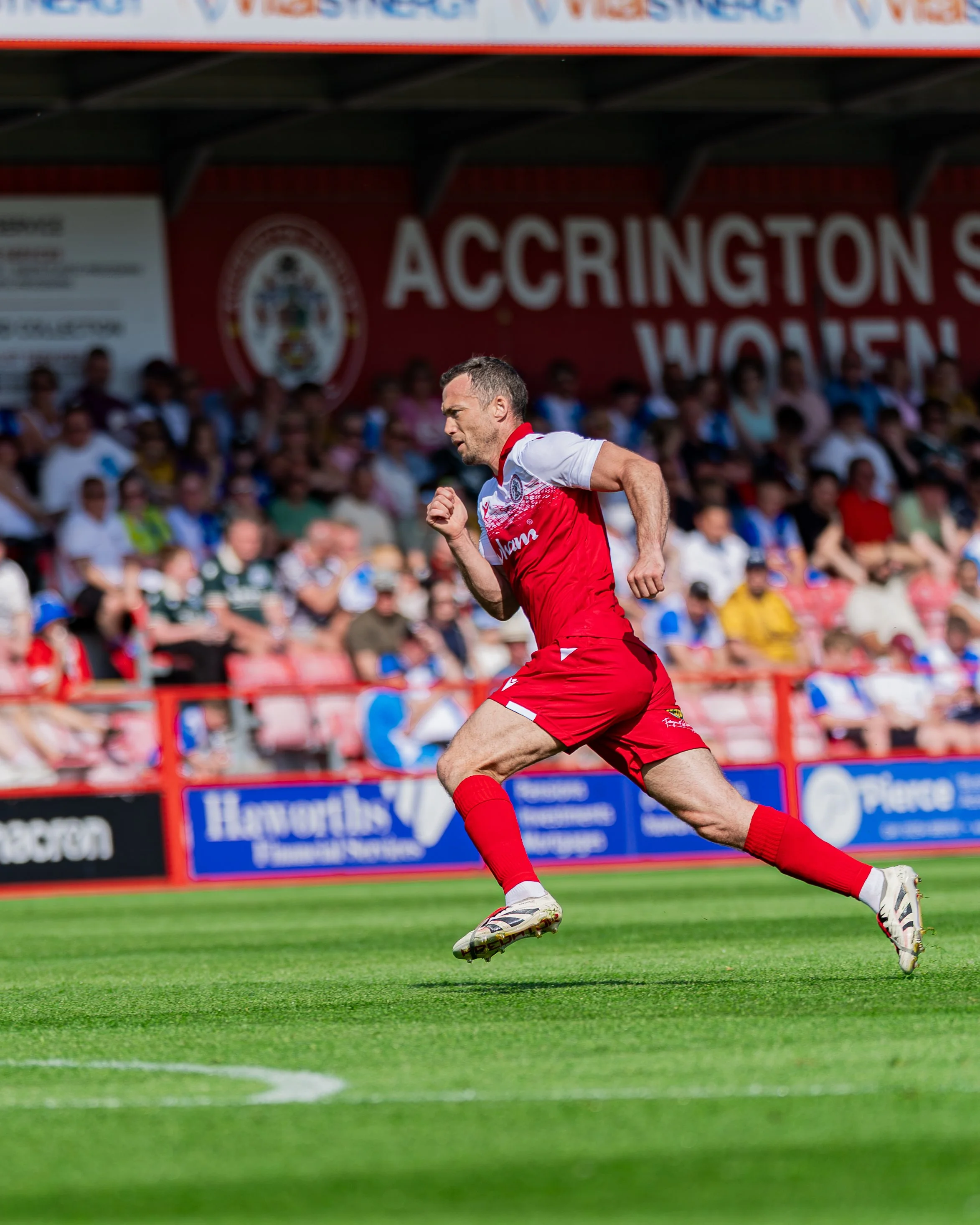 A man wearing a red and white sports uniform running on a soccer field during a match, with a crowd of spectators in the background.