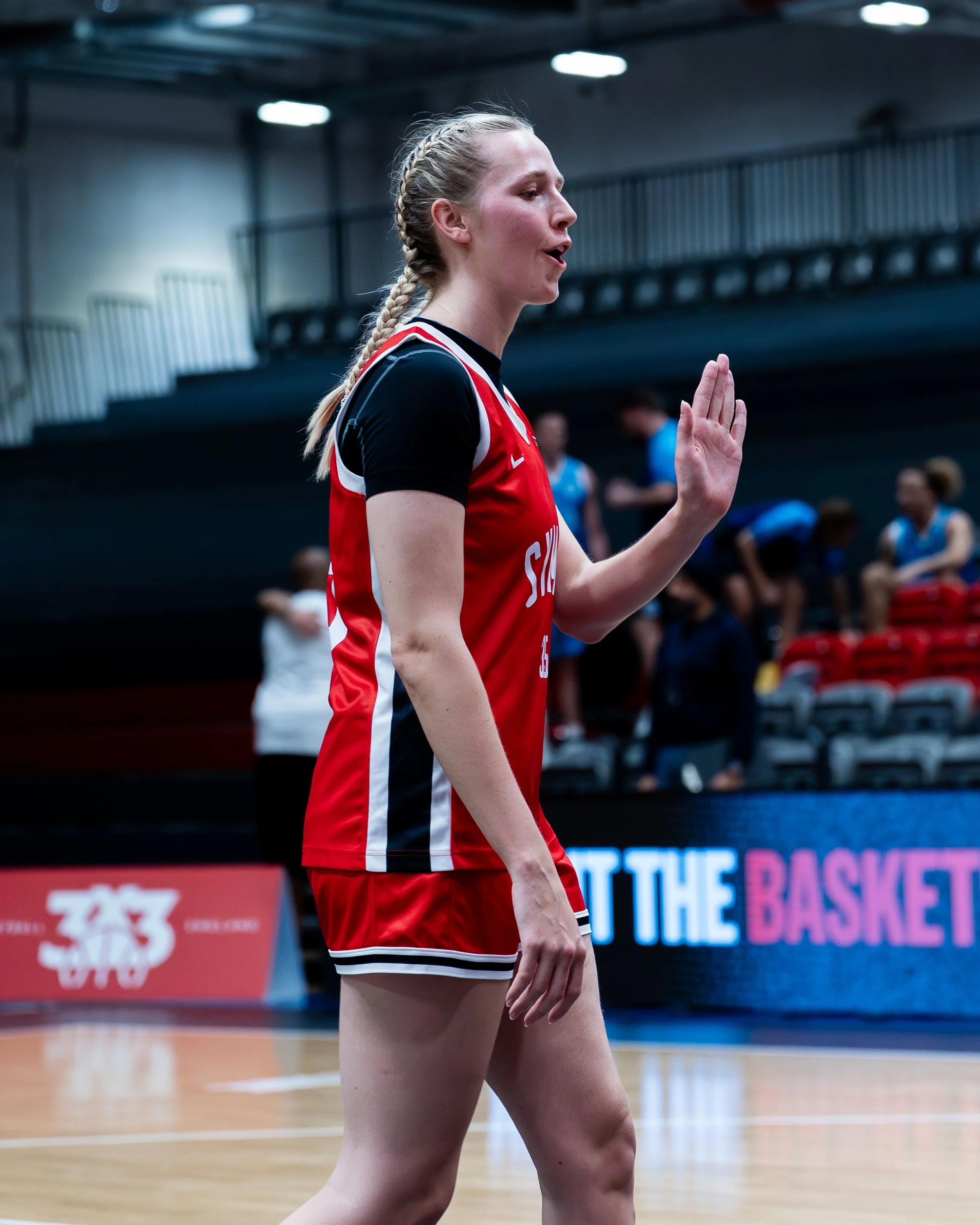 A female volleyball player in a red and black uniform standing on an indoor court with her right hand raised, likely during a match or practice.