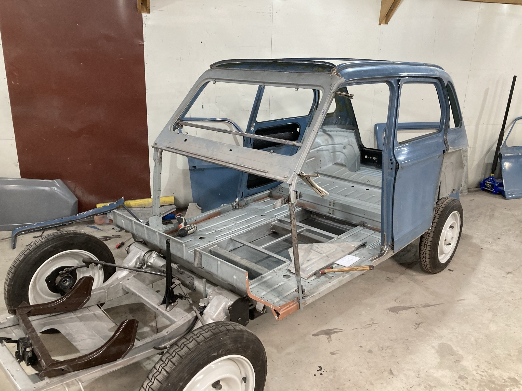 The image shows a partially assembled vintage pickup truck frame inside a garage or workshop, with some tools and parts nearby.