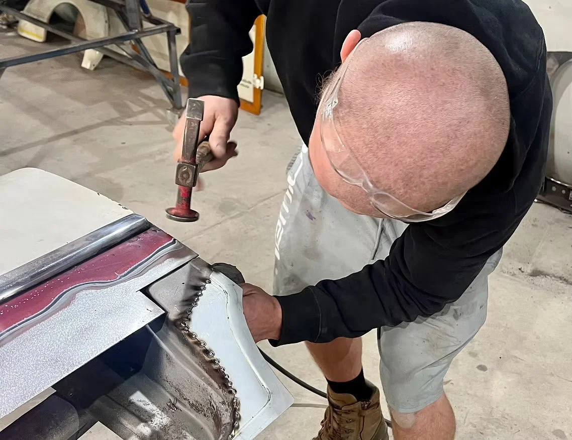 A person using a hammer and welding equipment to work on a metal structure in a workshop.