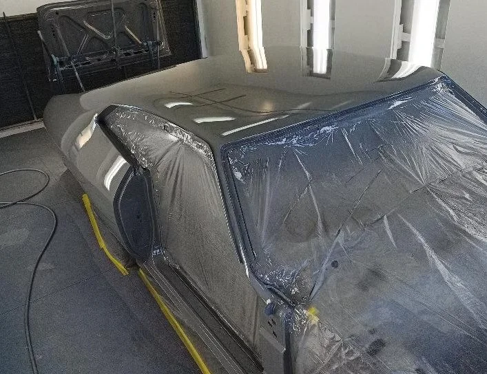 Silver car in a garage, covered in protective plastic wrap with a damaged windshield, situated on a yellow lift or platform.