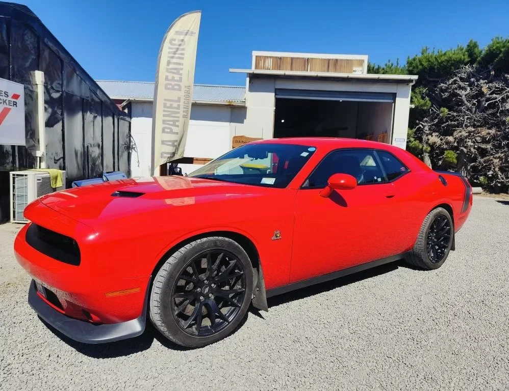 Red Dodge Challenger sports car parked outdoors on a sunny day.