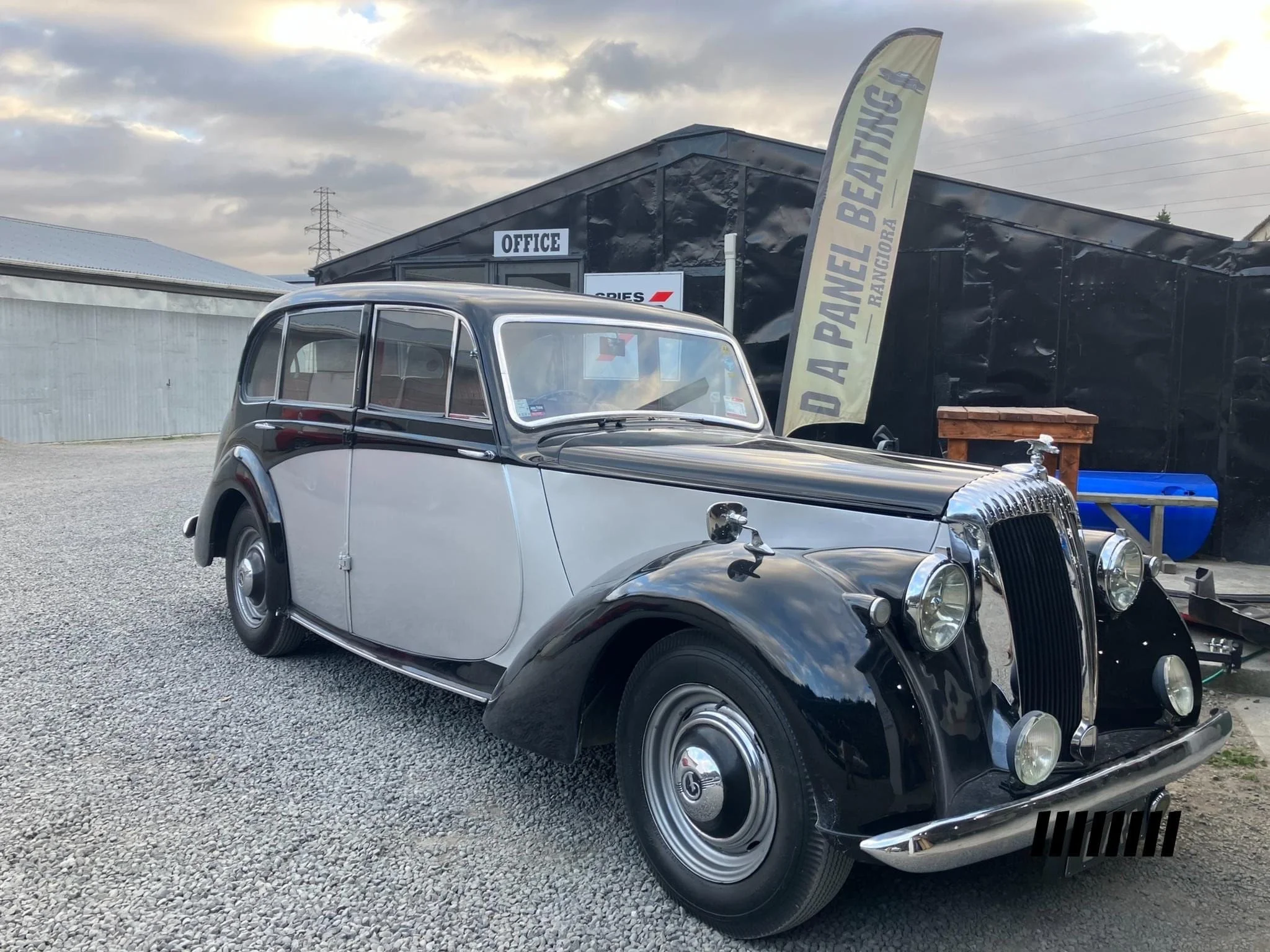 A vintage black and silver car parked outside a building with a sign that says 