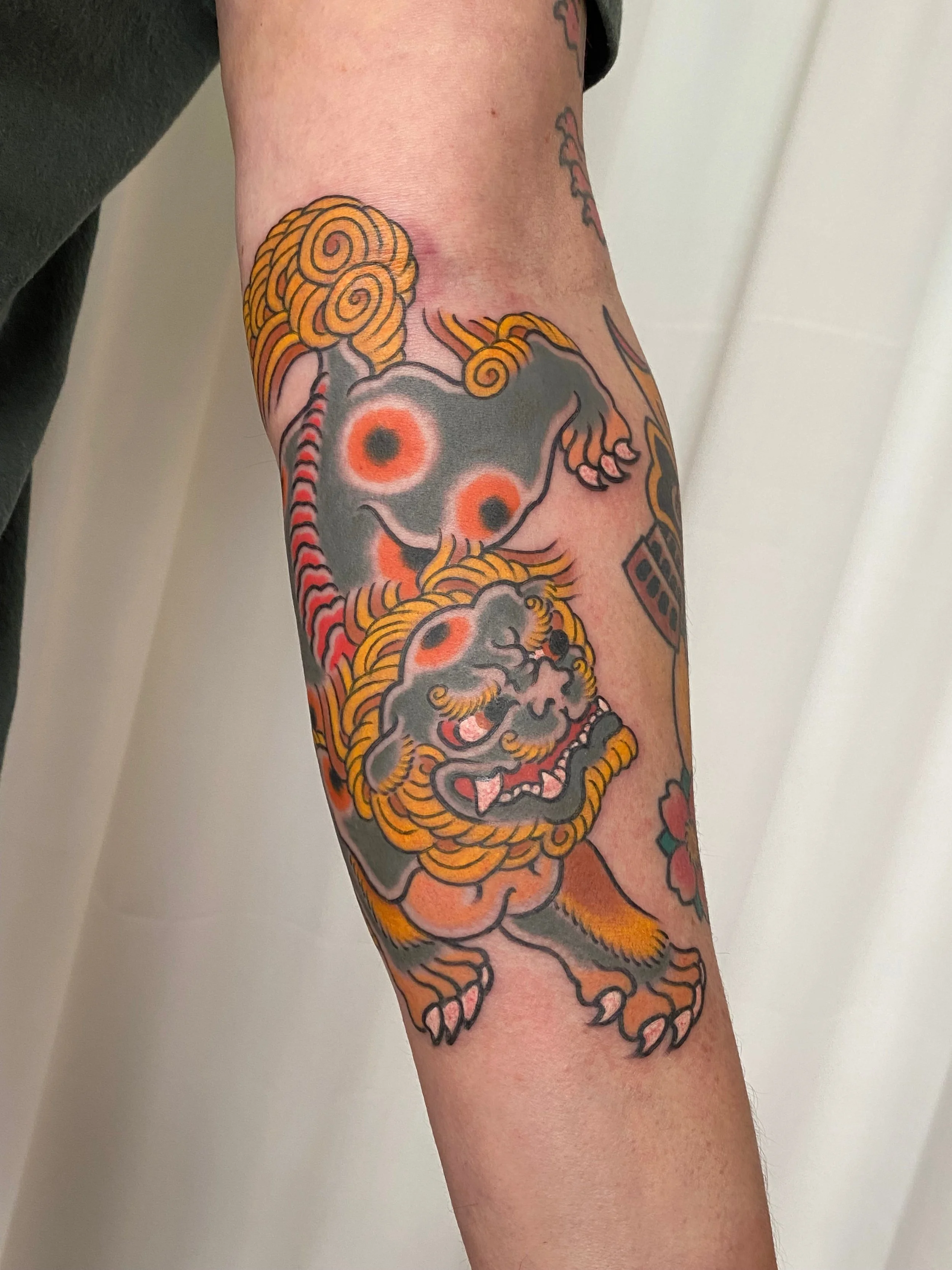 Traditionele Japanse draken-tatoeage op onderarm met zwarte, oranje en gele kleuren.
