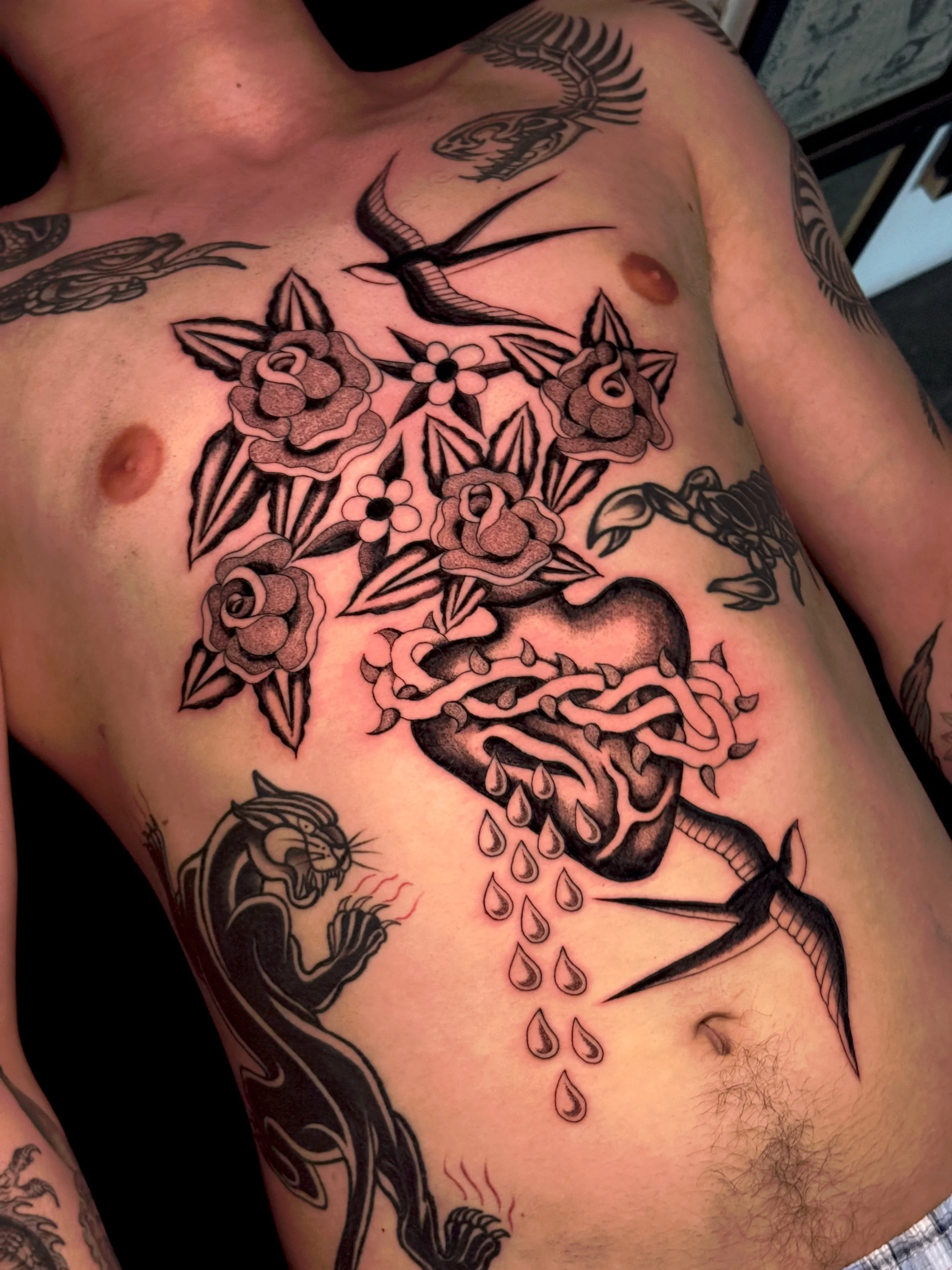 Tatoeage van een bloem, een vogel, een hart en een slang op een man's borst met een donkere achtergrond.