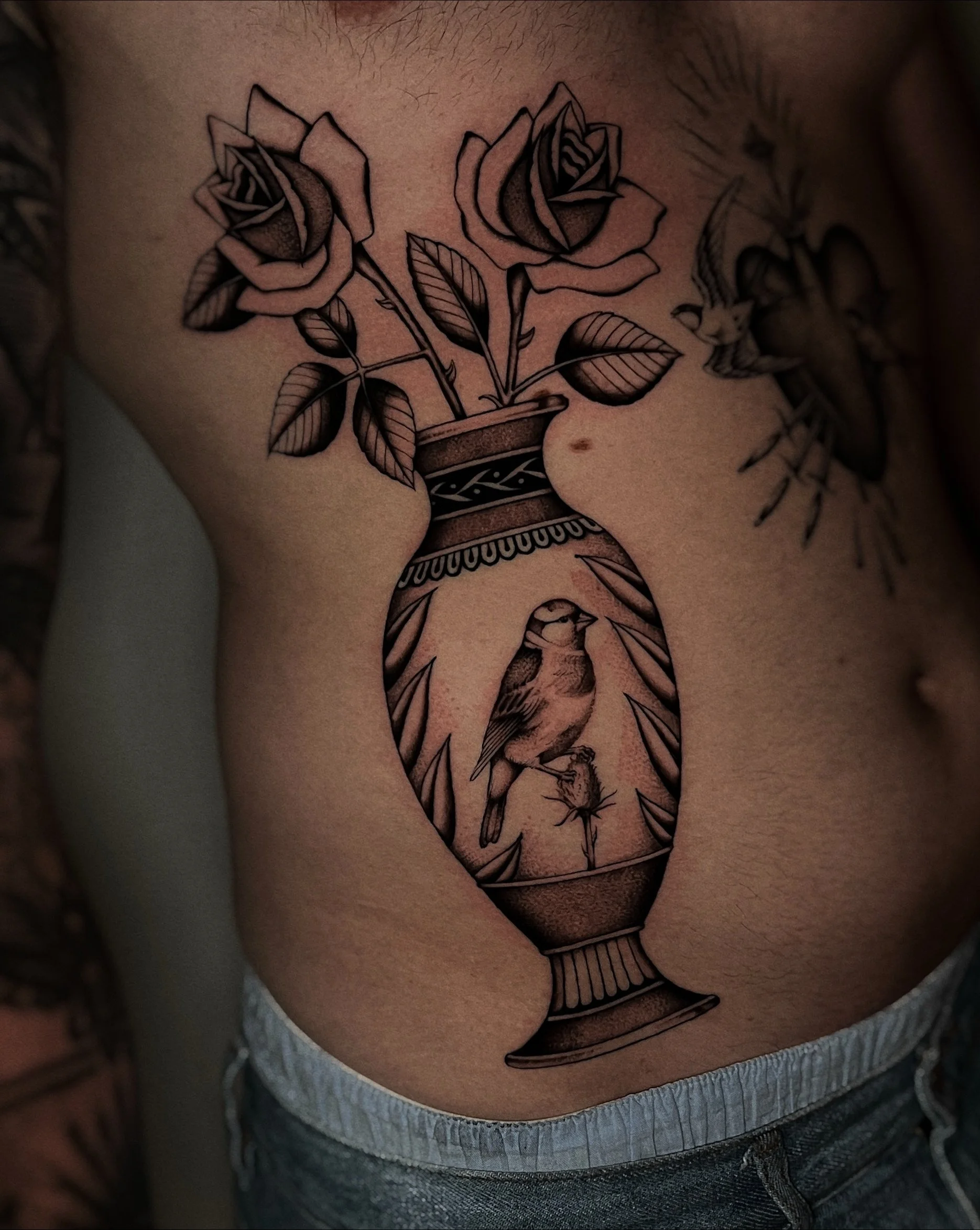 Tatoeage van een met een bloem en een vaas op de borst van een persoon.