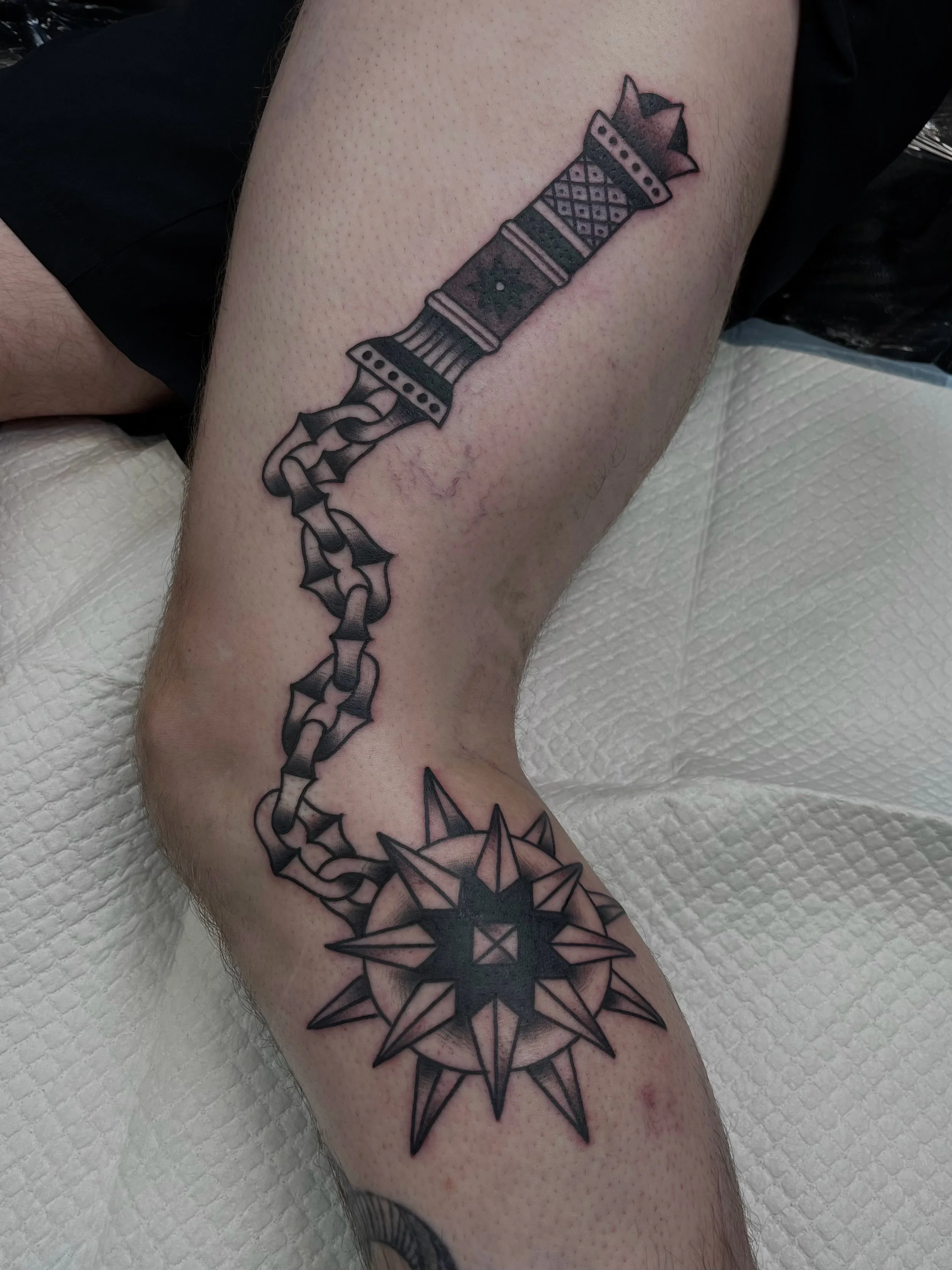 Tatoeage van een grote zwarte ster met pijlen en lijnen op een onderbeen.