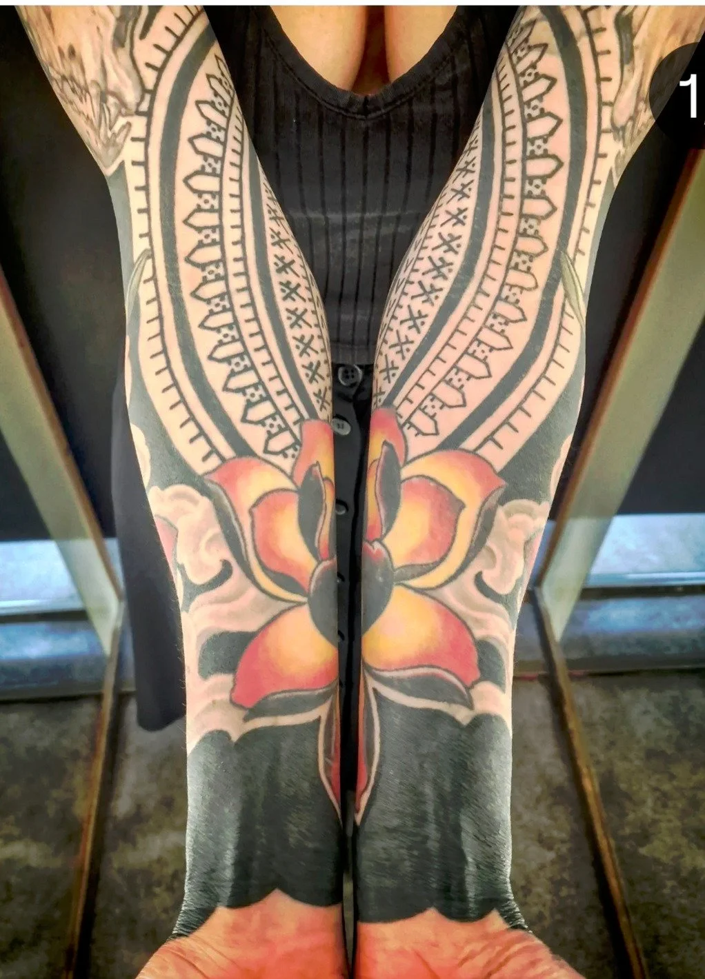 Een persoon met uitgebreide tattoo's op armen en onderrug, gekleed in een zwart gestreept topje, neemt een selfie voor een spiegel.