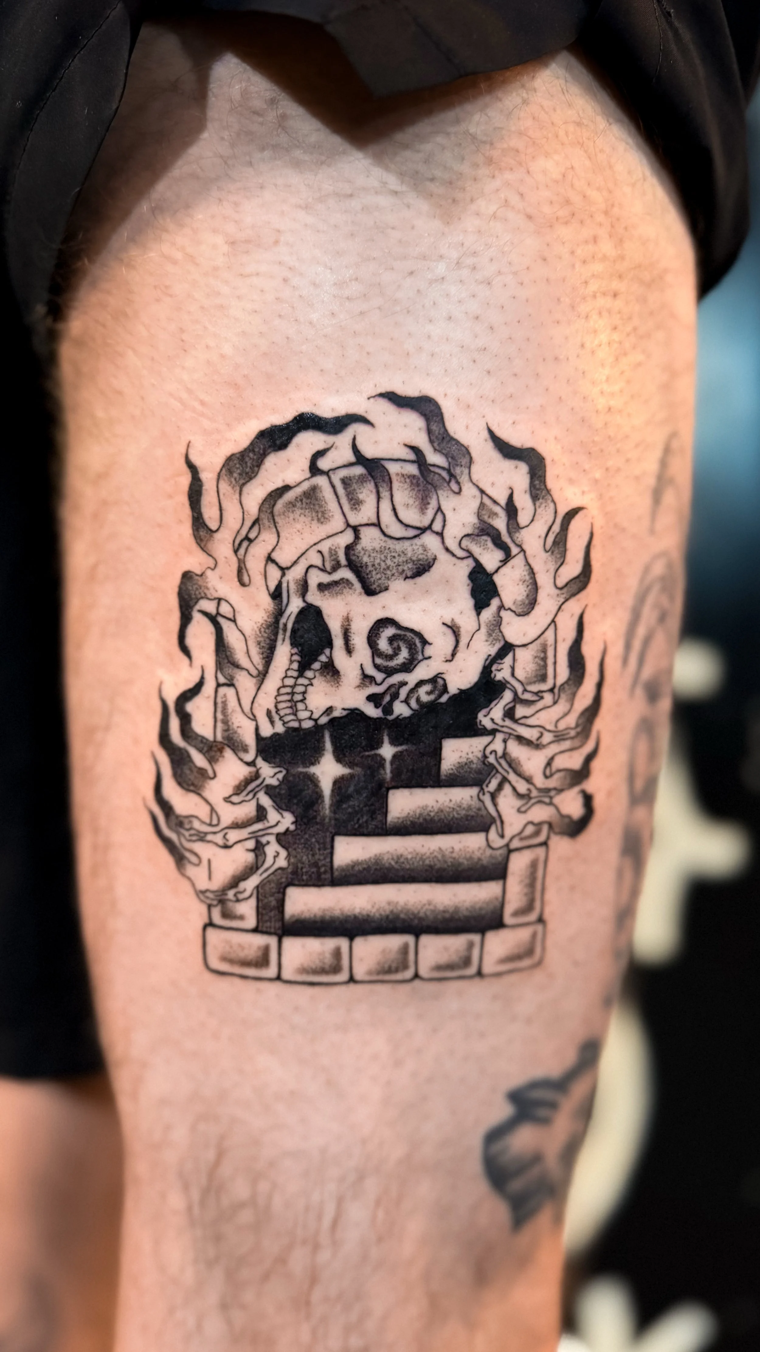 Tattoo van een schedel met rookpatronen op de bovenarm, met een trap en sterren eronder.