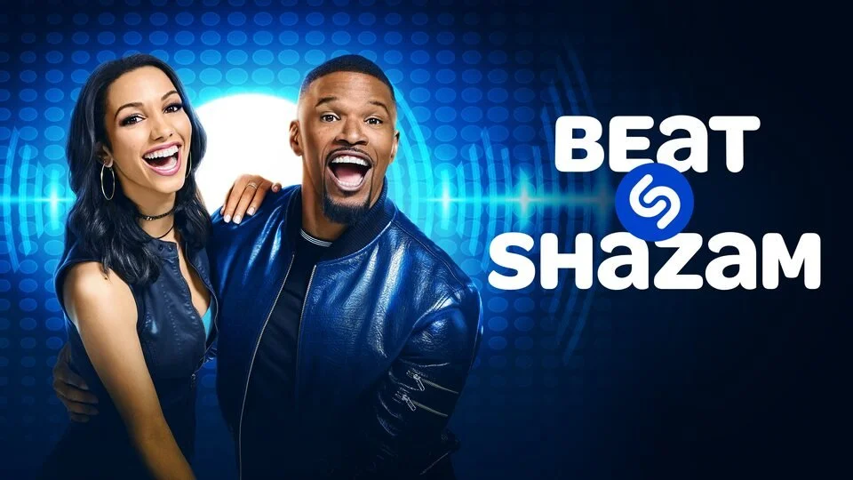 A man and woman posing together, smiling, with a graphic background featuring a Beat Shazam logo and soundwave patterns.