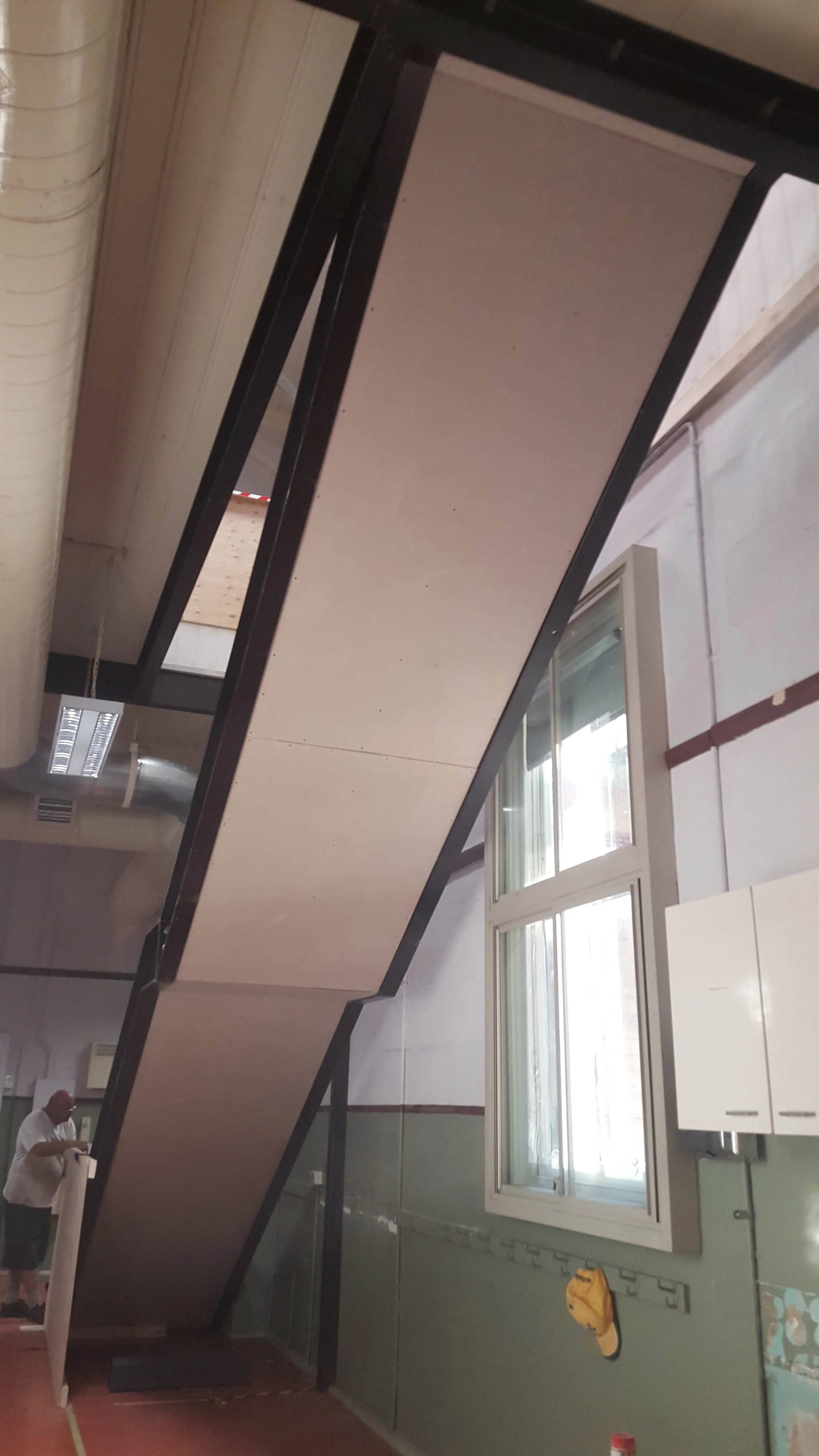 Indoor basketball court with a backboard and hoop, large window, and a person standing near the net.