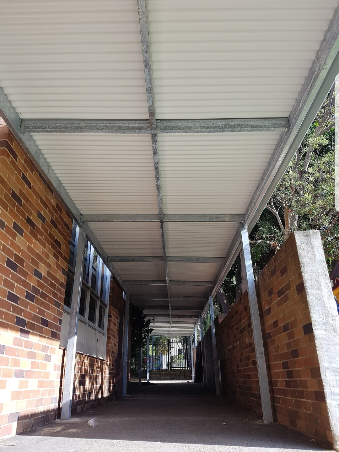 Covered walkway with brick walls and a metal roof, leading to a gated outdoor area.