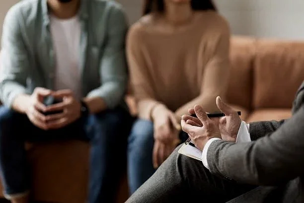 A therapist conducting a session with a couple, sitting on a sofa in a therapy office.