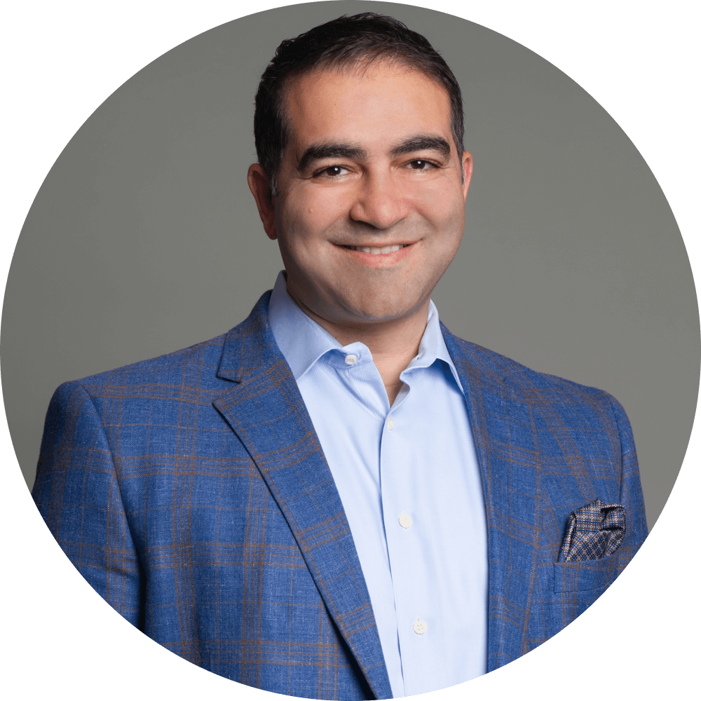 A professional man in a blue checked blazer and light blue shirt, smiling against a grey background. Member of the AI Aptitude Institute Advisory Board and expert in enterprise AI strategy