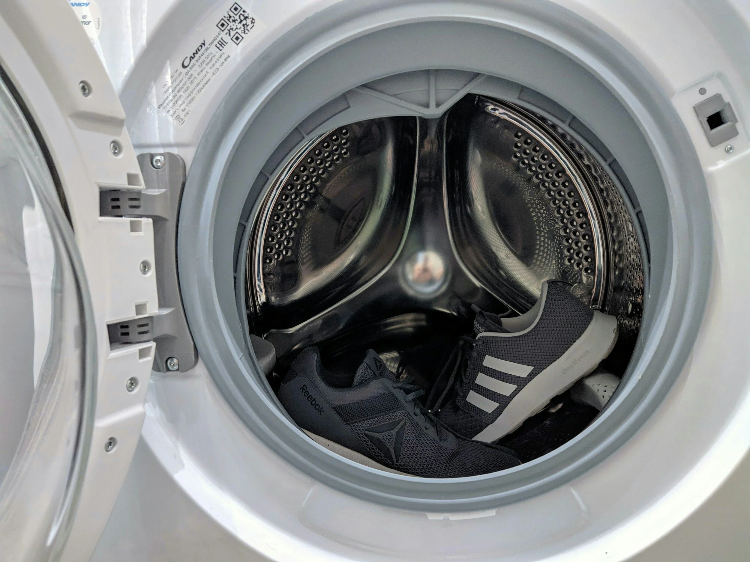 Front view inside a washing machine drum with black Reebok sneakers placed inside.