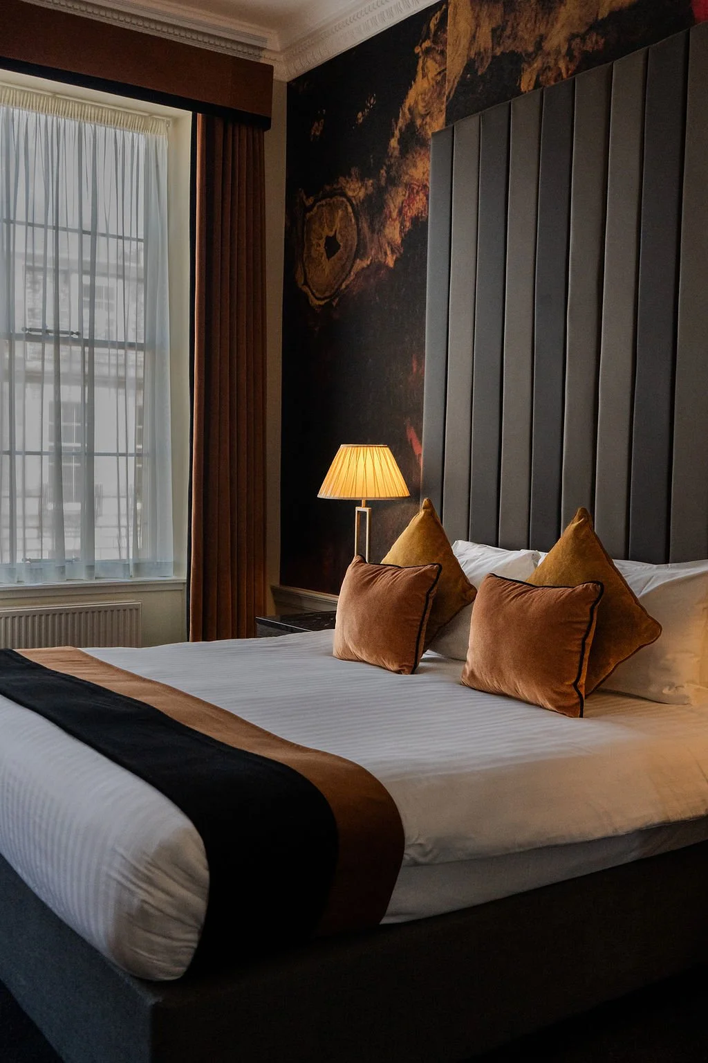 A neatly made bed with white pillows and bedding in a hotel room, viewed through a partially opened door.