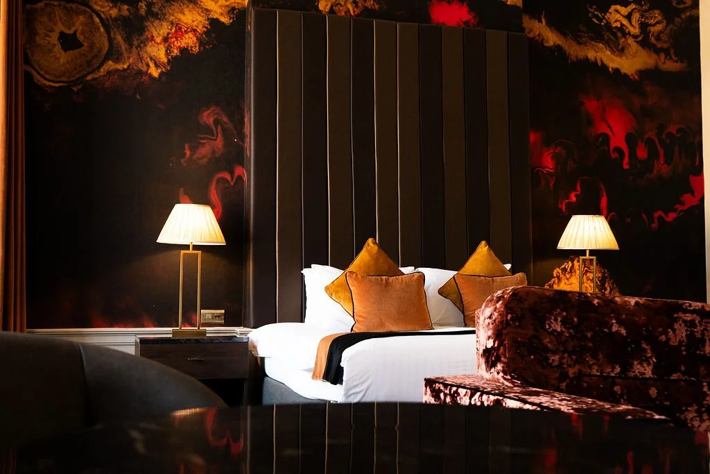 View of a neatly made bed with white pillows and bed sheets, framed by blurred parts of a hotel room inside a hotel room