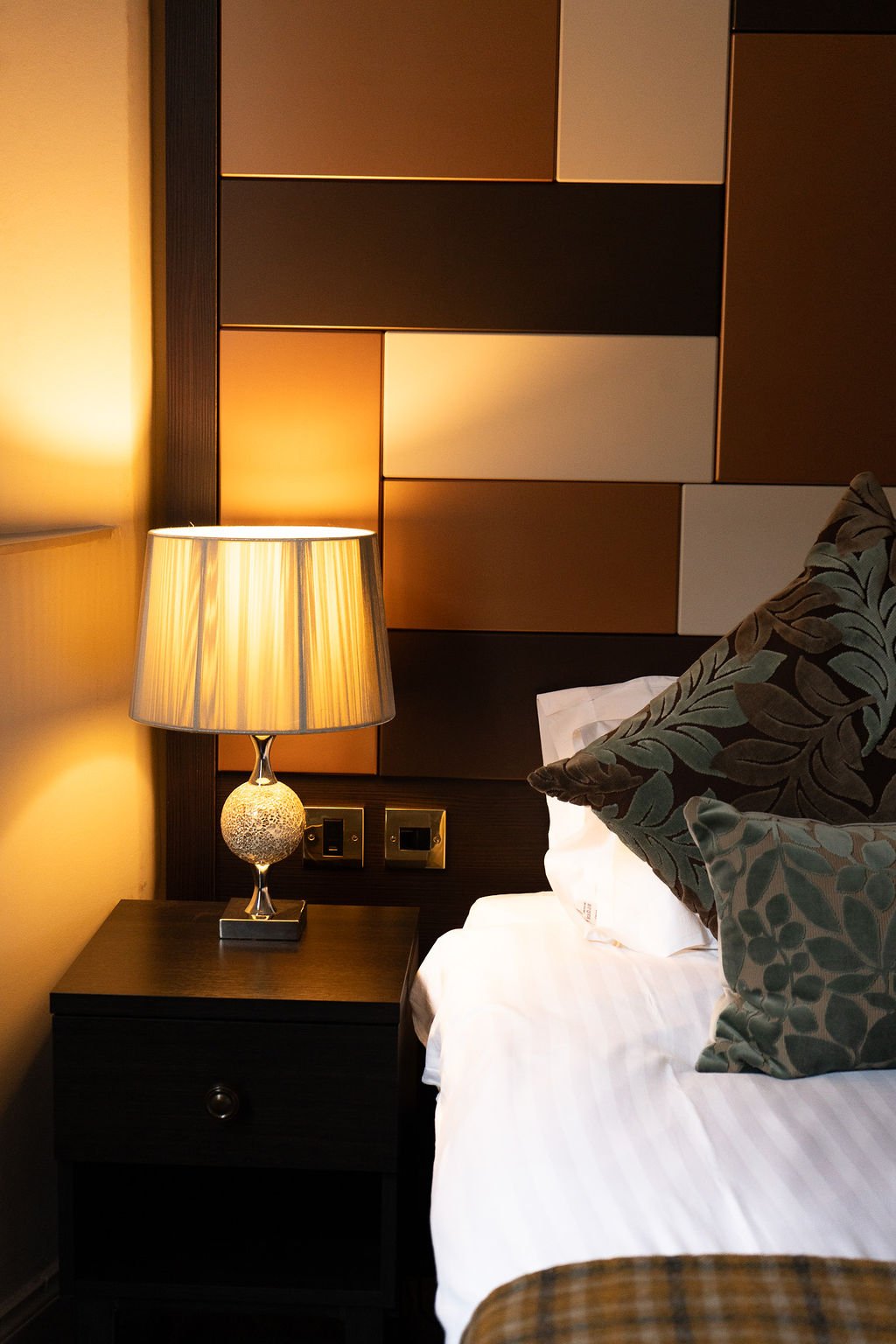 A neatly made bed with white pillows and sheets, viewed through a door or frame in a hotel room.