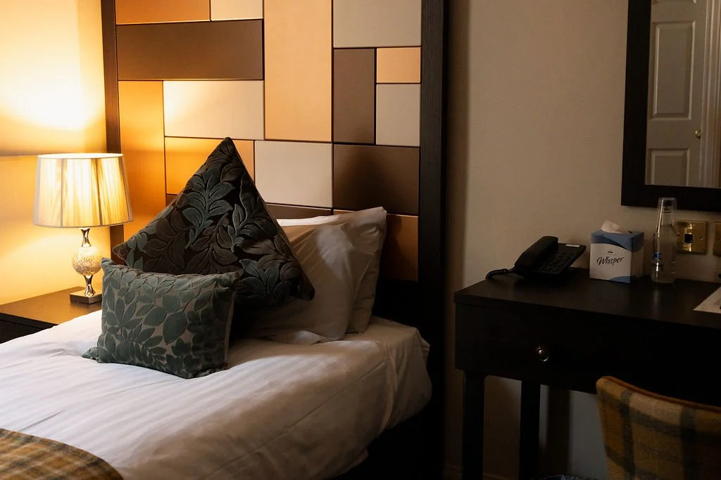 A neatly made bed with white pillows and bed linens, viewed through a small opening suggesting a peephole or a narrow frame.