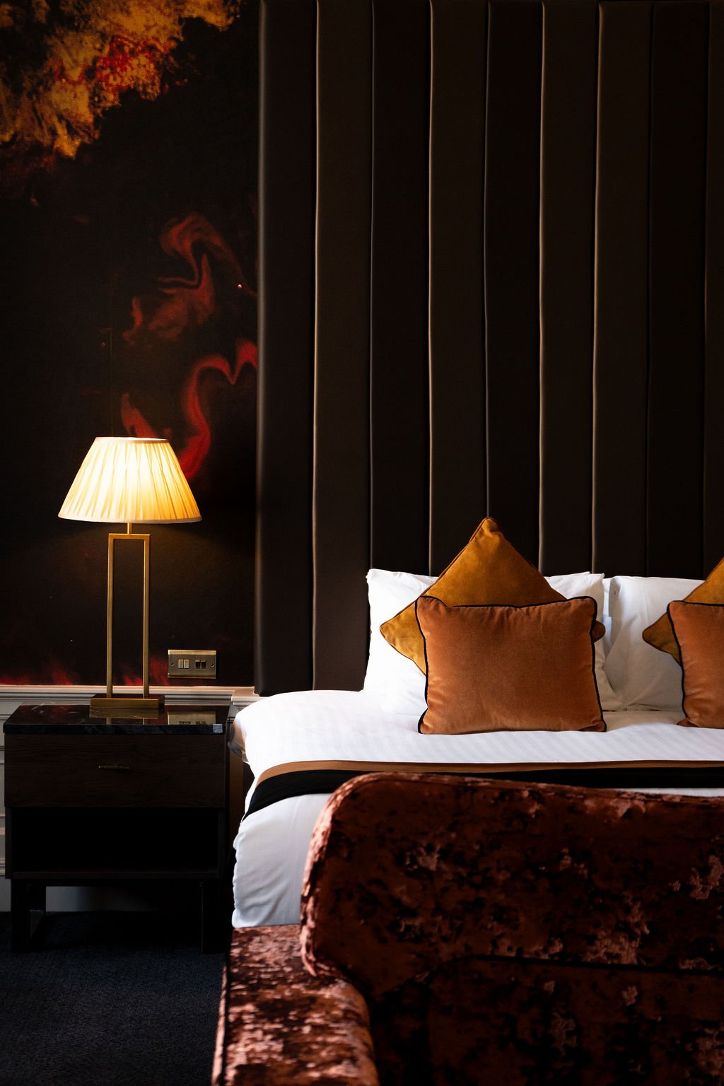 A neatly made bed with white pillows and sheets, viewed through a partially opened door or window, with a dark wooden headboard and a wall-mounted lamp.