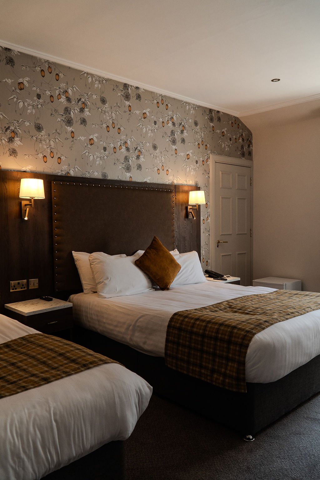 View of a neatly made bed with white pillows and bed sheets, framed by blurred parts of a hotel room inside a hotel room
