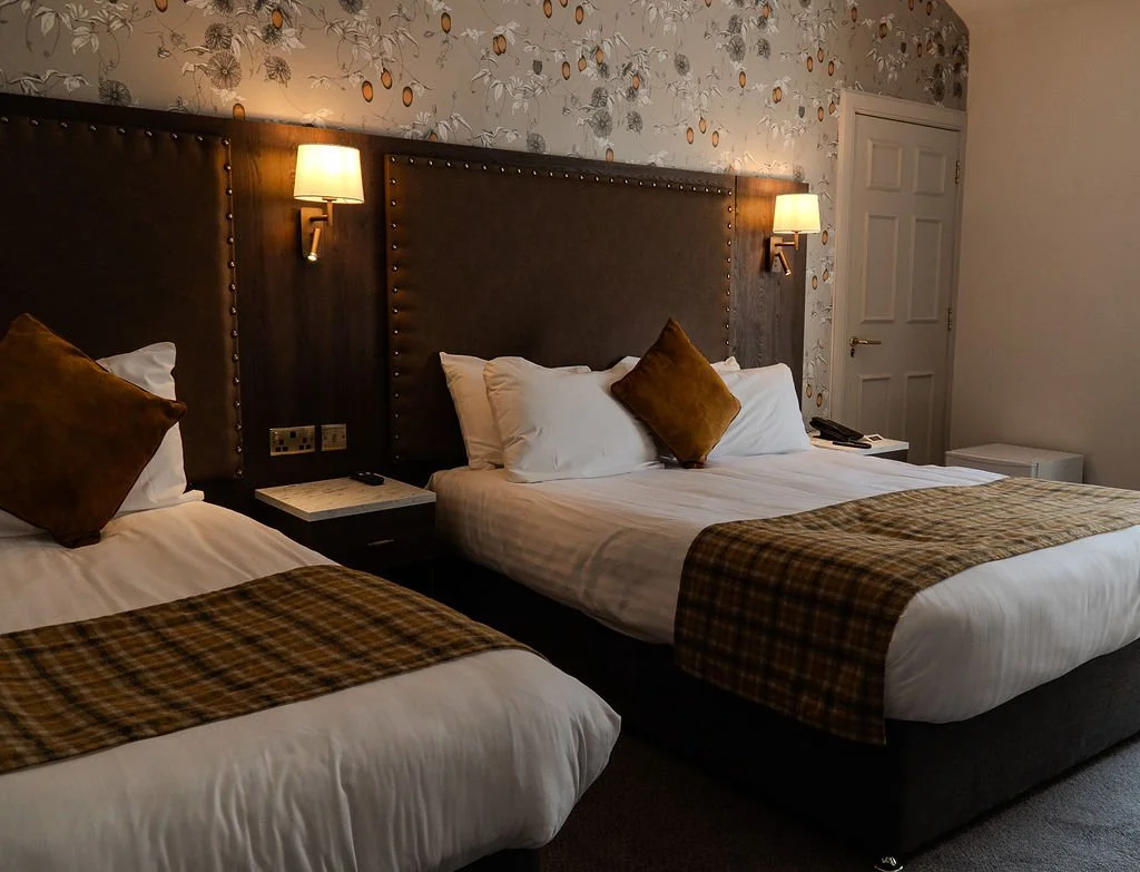 A neatly made hotel bed with white pillows and bedding, viewed through a partially opened door.