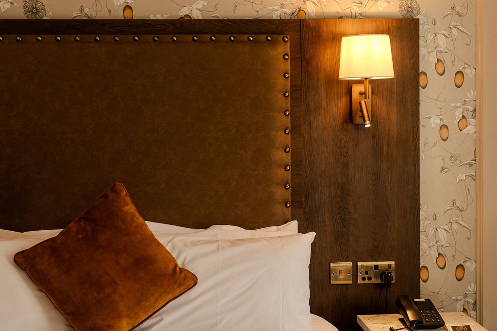 A neatly made bed with white pillows and bed linens, viewed through a small opening suggesting a peephole or a narrow frame.