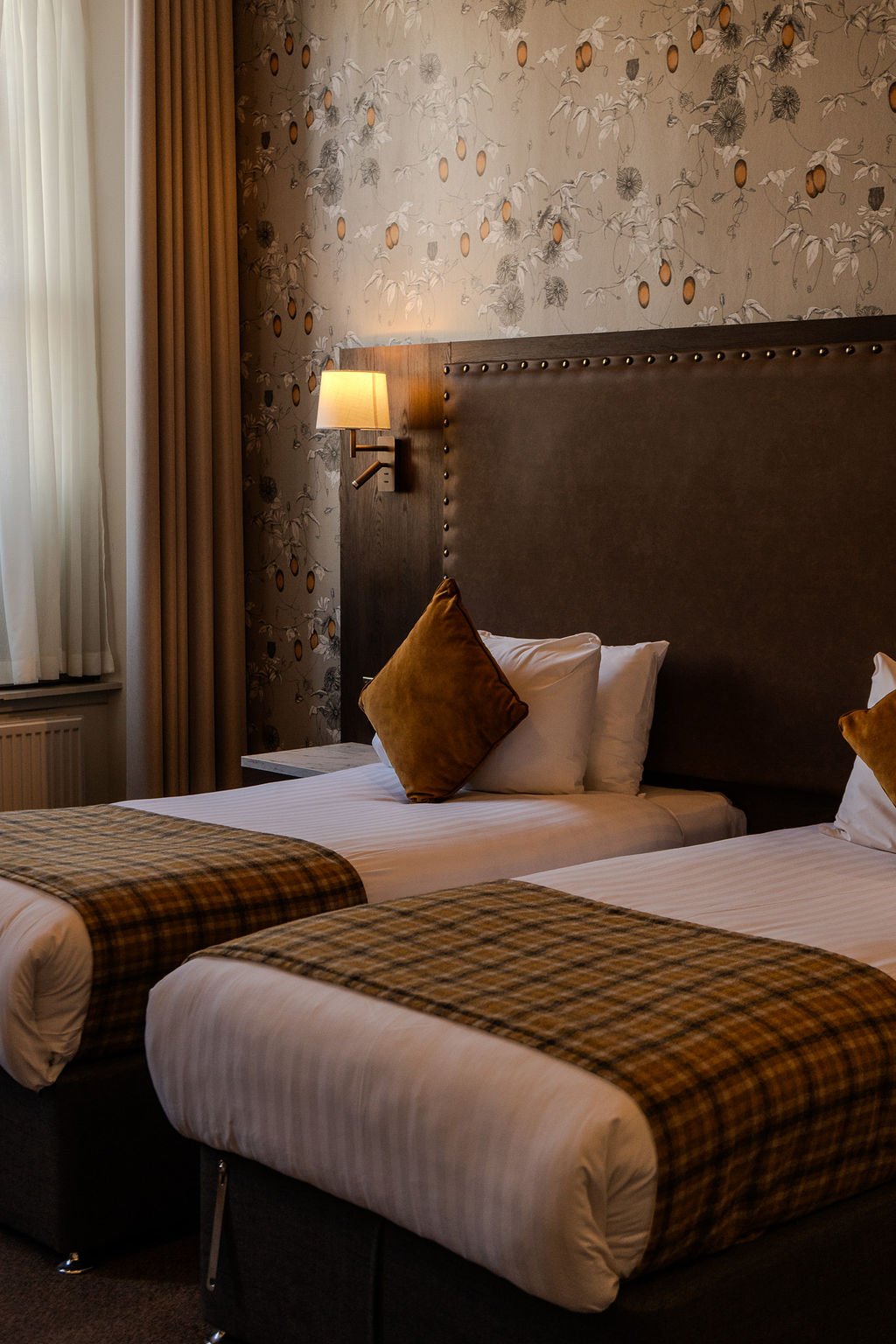 View of a neatly made bed with white pillows and bed sheets, framed by blurred parts of a hotel room inside a hotel room