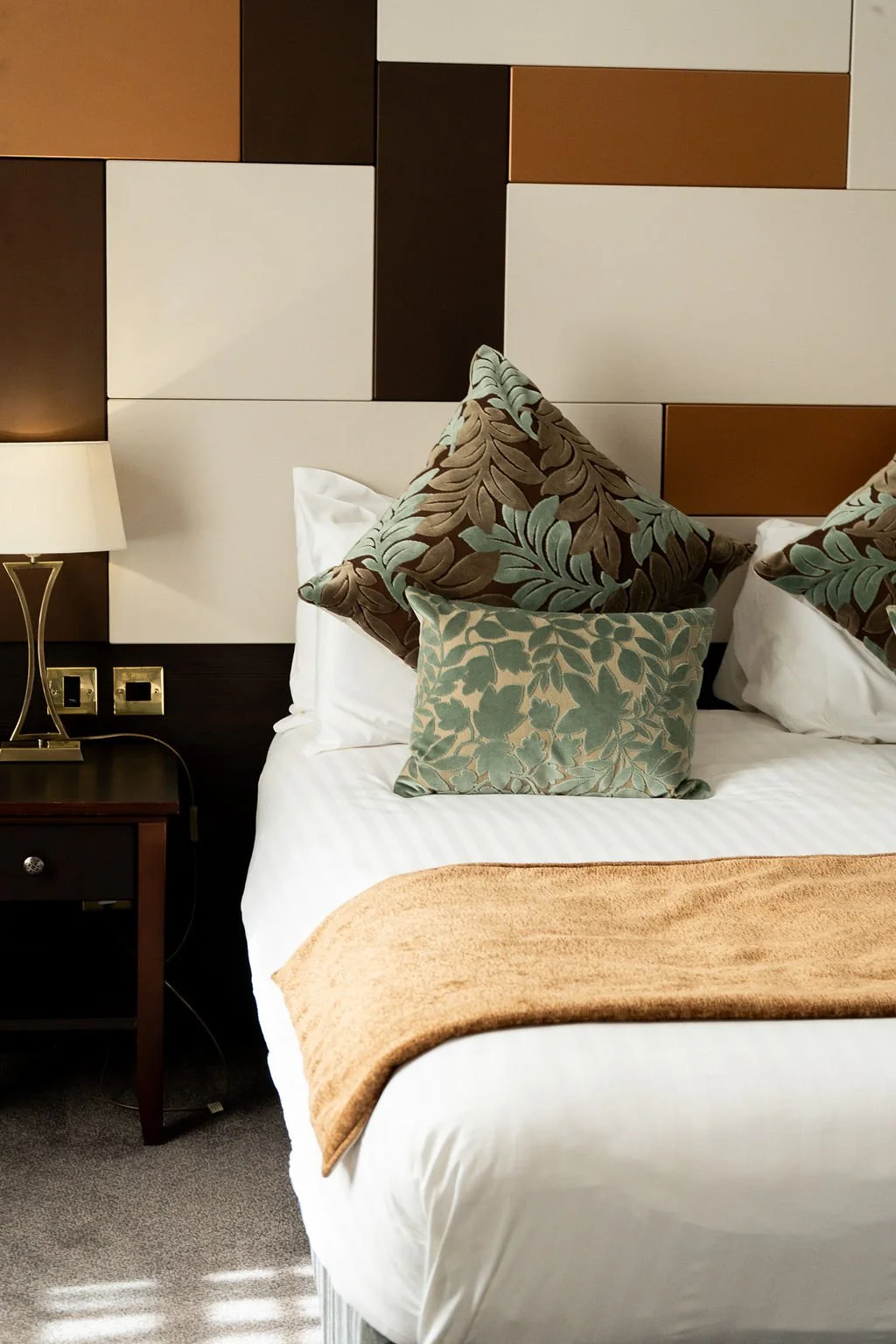View of a neatly made bed with white pillows and bed sheets, framed by blurred parts of a hotel room inside a hotel room