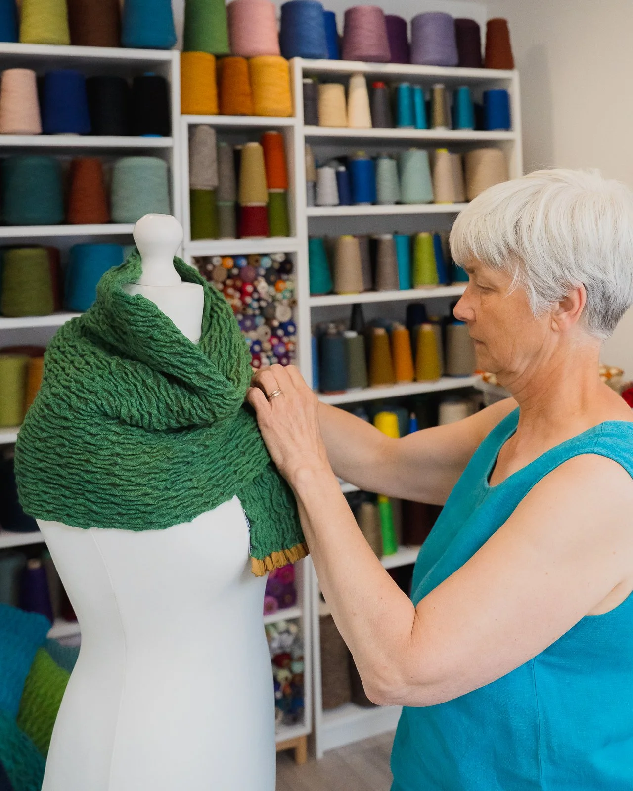 Suzanne Townshend at Treadle Lightly placing handwoven green scarf on mannequin