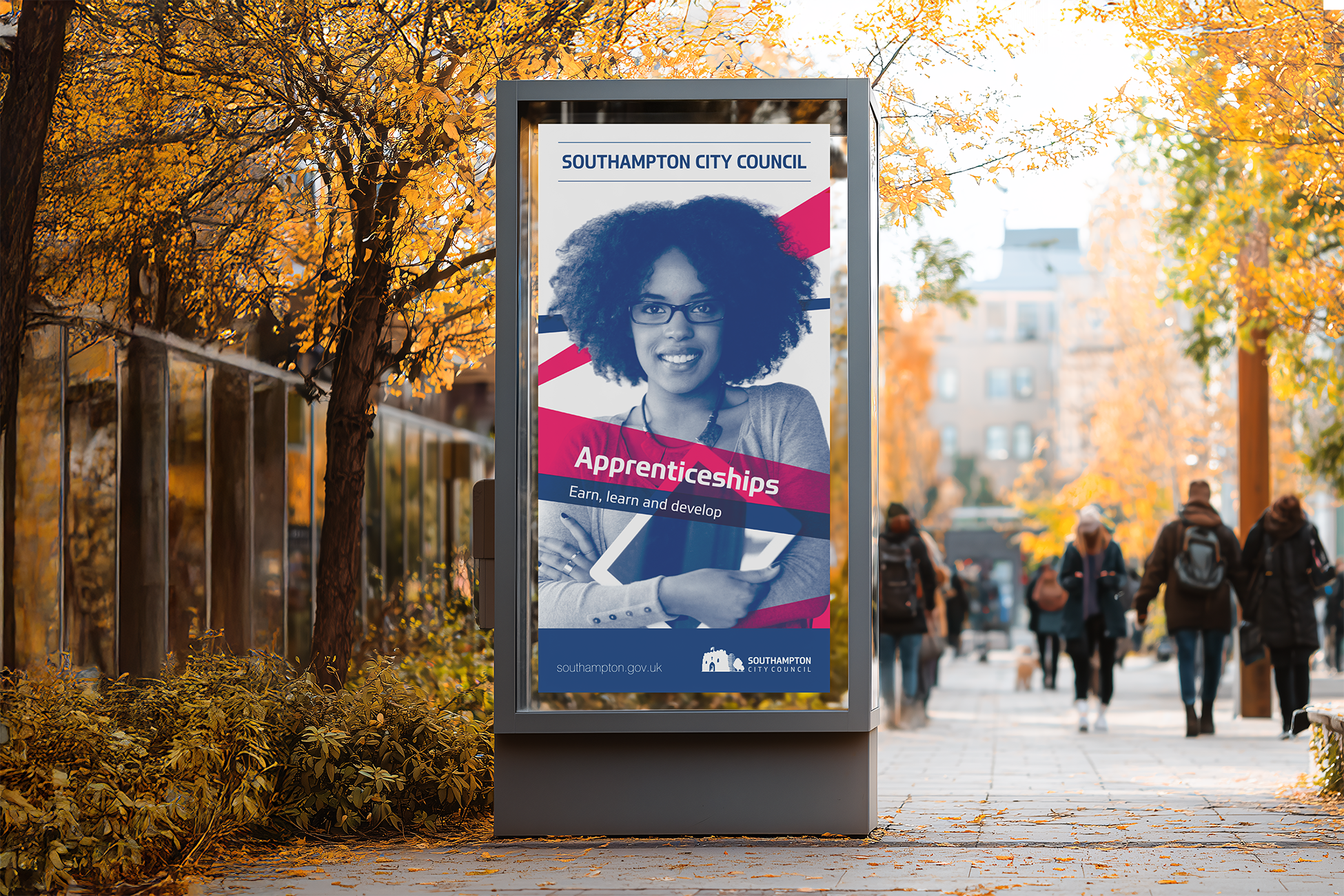 Outdoor advertisement for Southampton City Council promoting apprenticeships, featuring a smiling woman with curly hair and glasses holding a tablet, set against autumn foliage and city buildings.