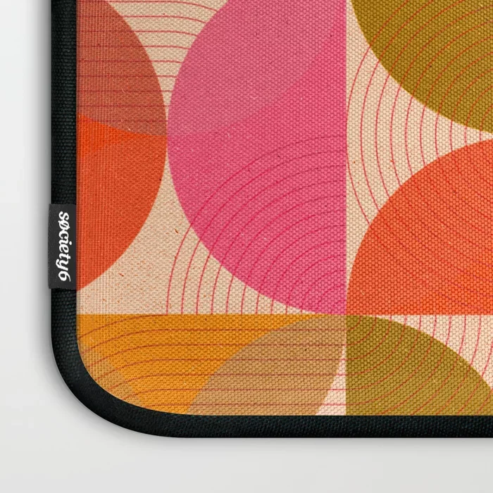 Society6 – art print. Close-up of a patterned desk mat with geometric circles in pink, orange, yellow, and green, with black edges and a brand label stating 'Society6'.