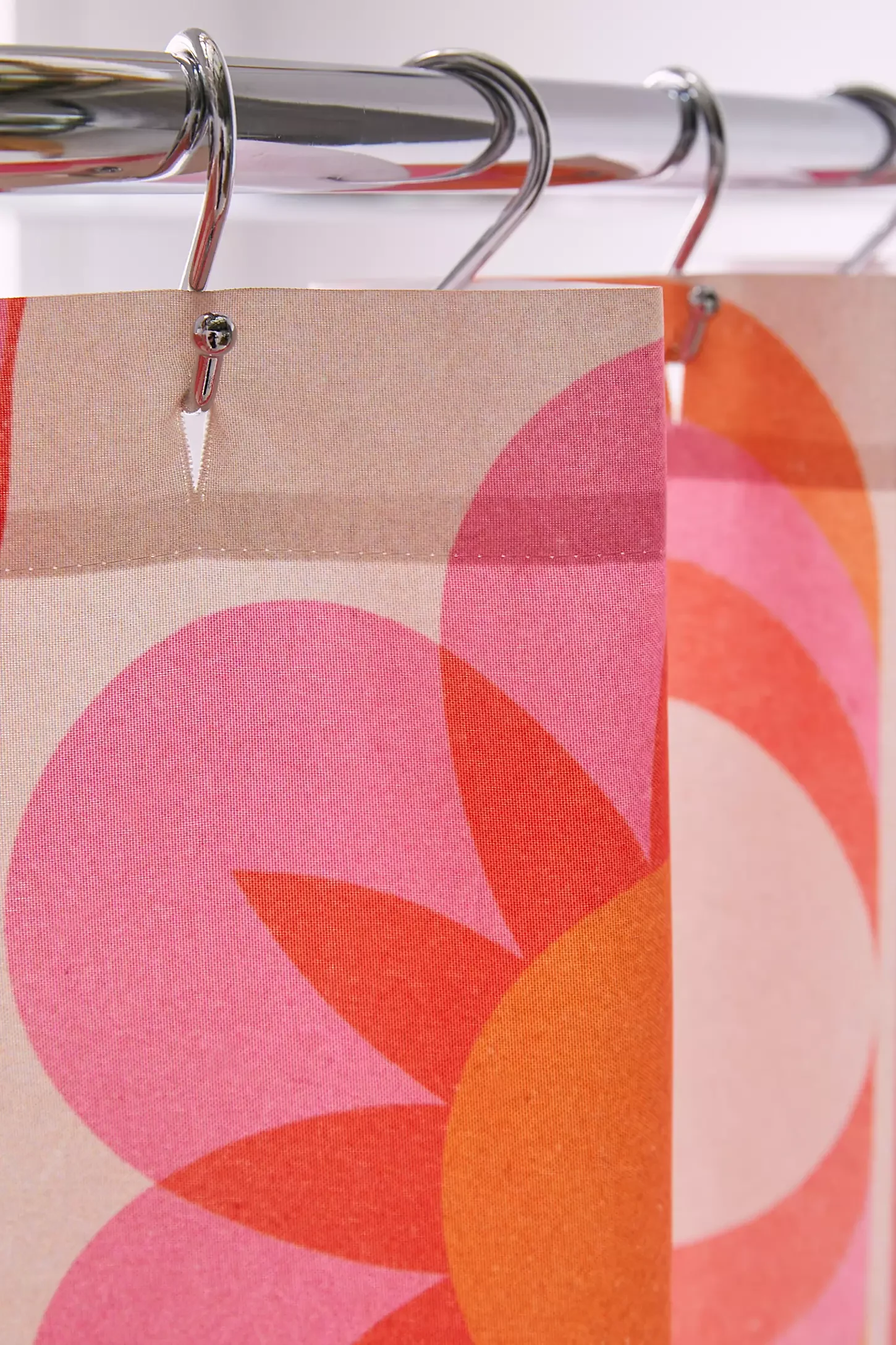 Close-up of patterned fabric with pink, orange, and beige colors, hanging on metal hangers from a metal rod.