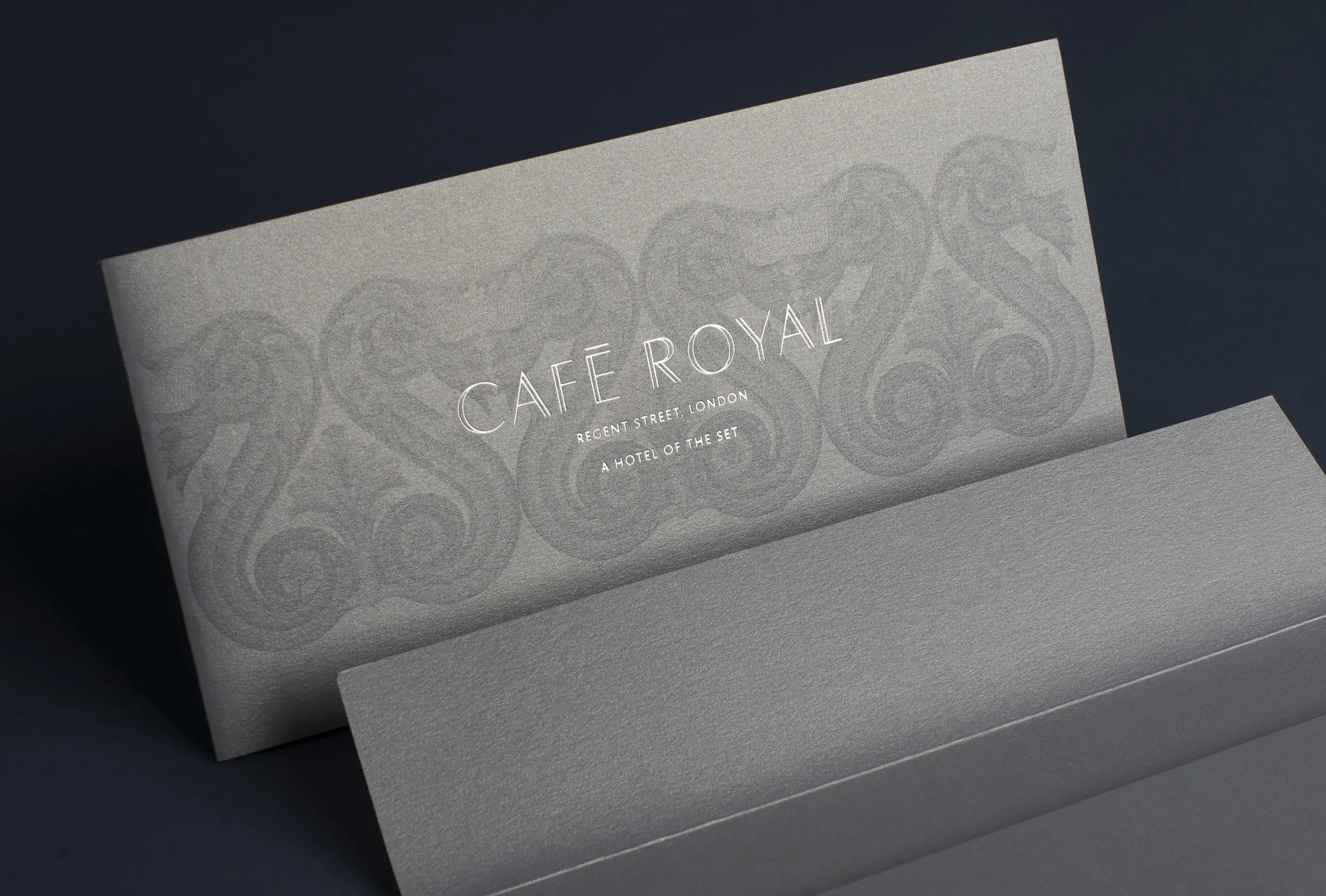 A grey envelope with the words 'CAFÉ ROYAL' printed in white, along with the address 'Regent Street, London' and 'A HOTEL OF THE SET'.