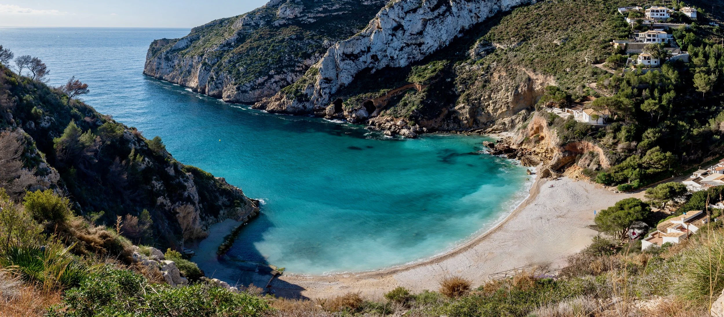 Baie de la Costa Blanca aux eaux turquoise, plage de sable blanc et maisons blanches sur les falaises.