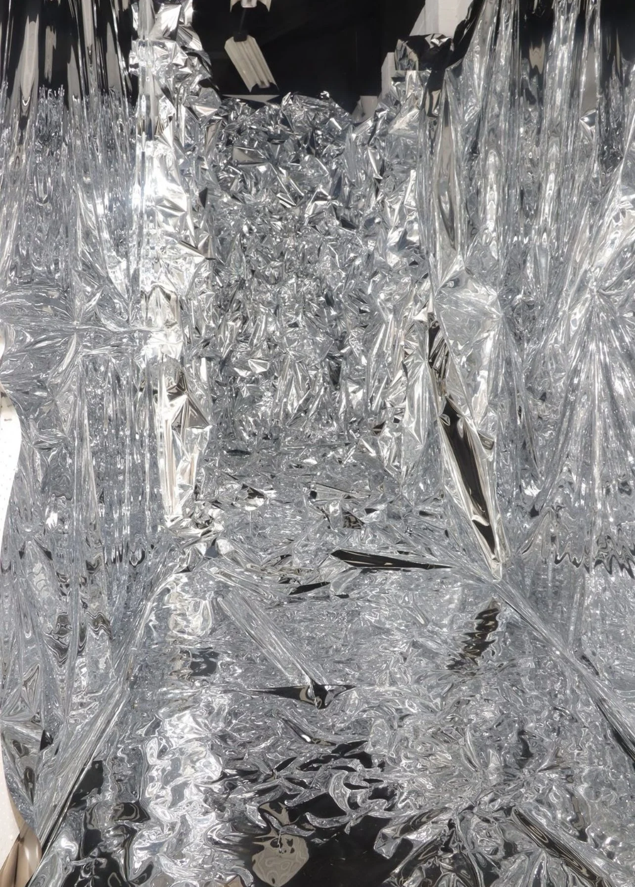 A room with walls, floor, ceiling and objects covered with crumpled and wrinkled reflective aluminum foil.