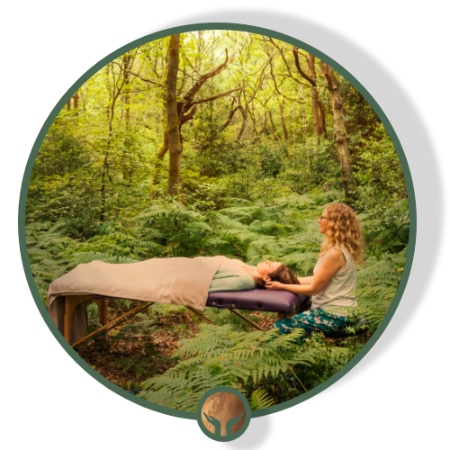 A woman receiving a massage outdoors in a lush green forest surrounded by trees and ferns